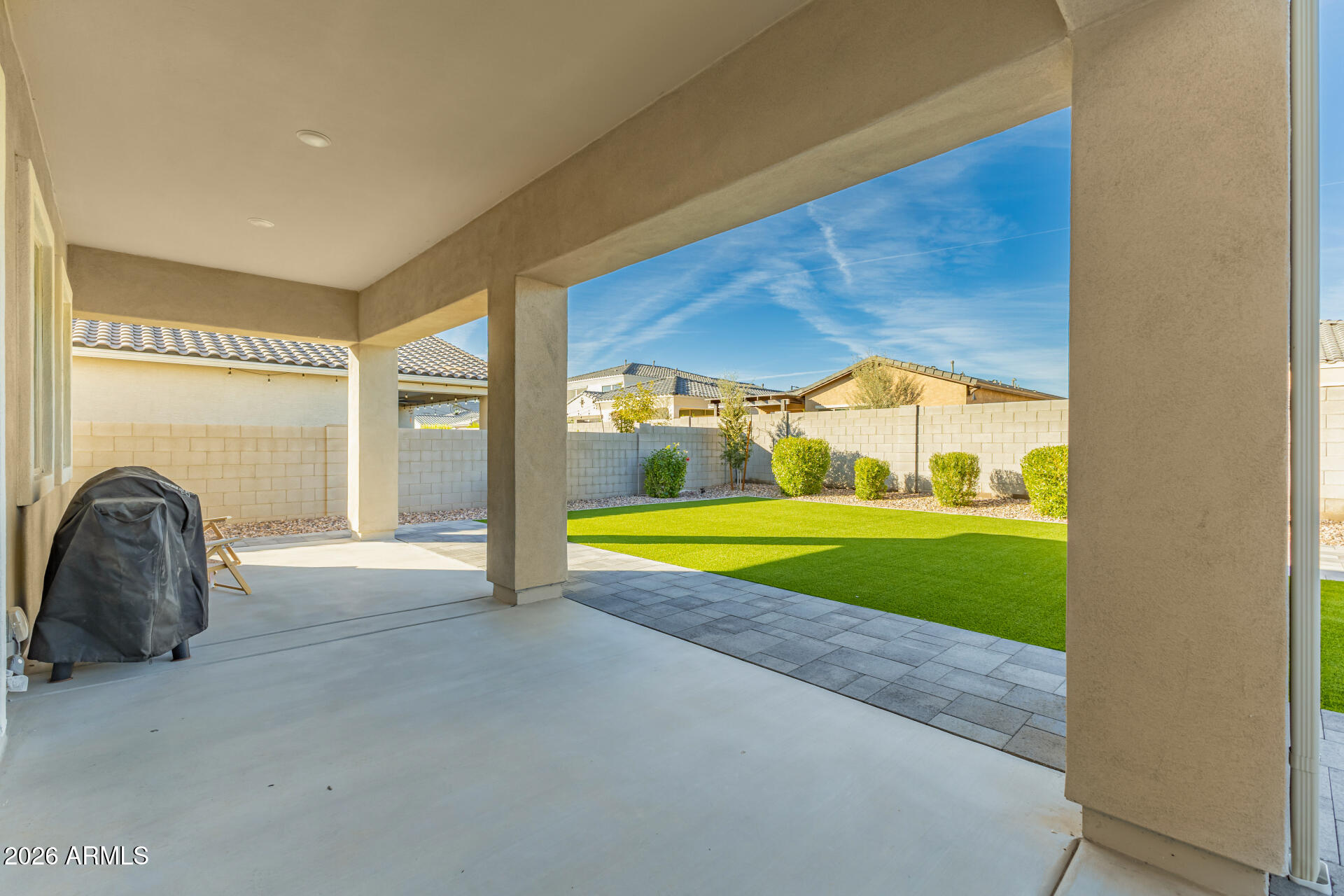 Covered patio overlooking a green backyard lawn, with a covered grill and paver border.