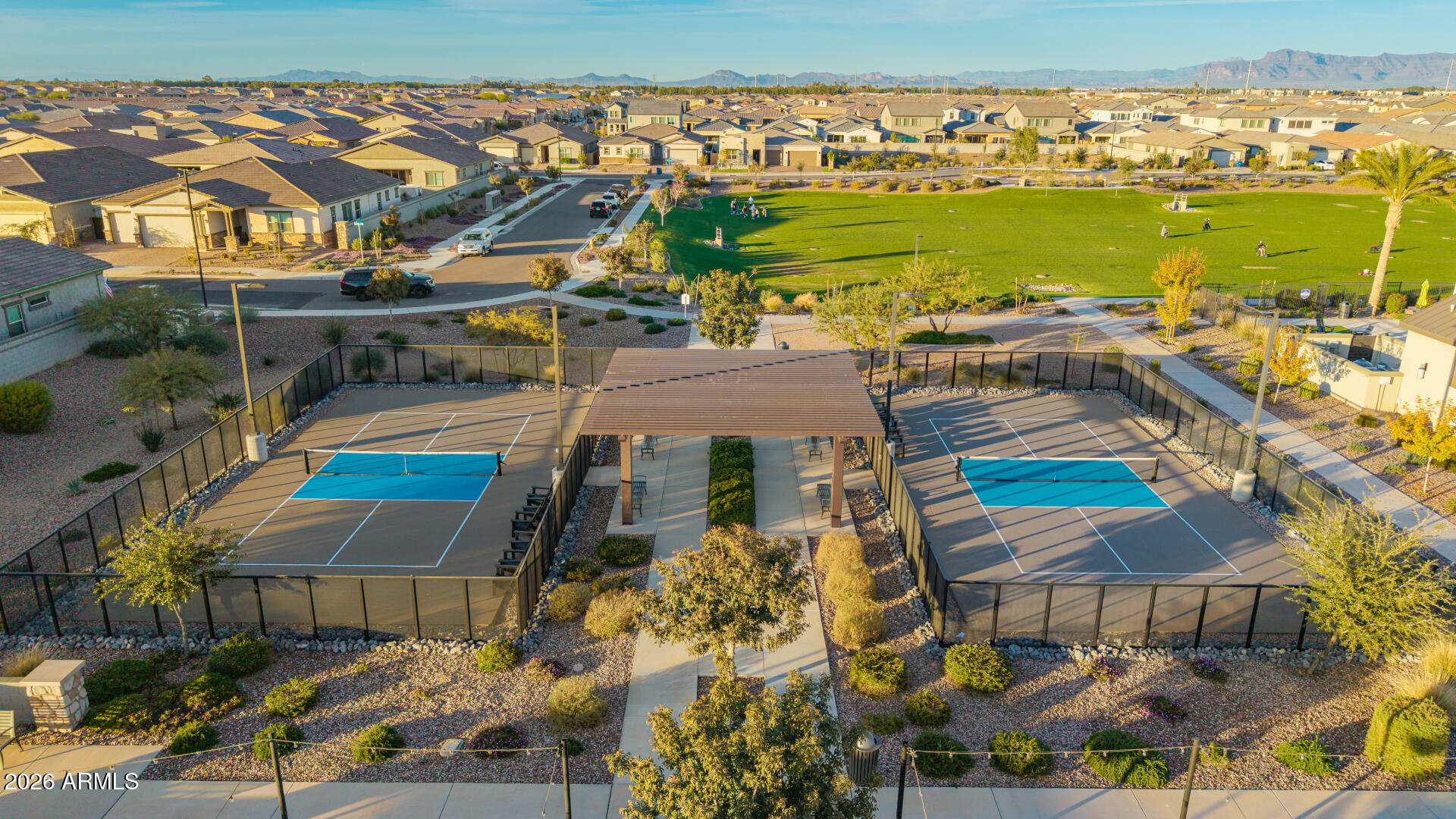 Aerial view of a neighborhood park with two pickleball courts, a broad lawn, and distant mountains.