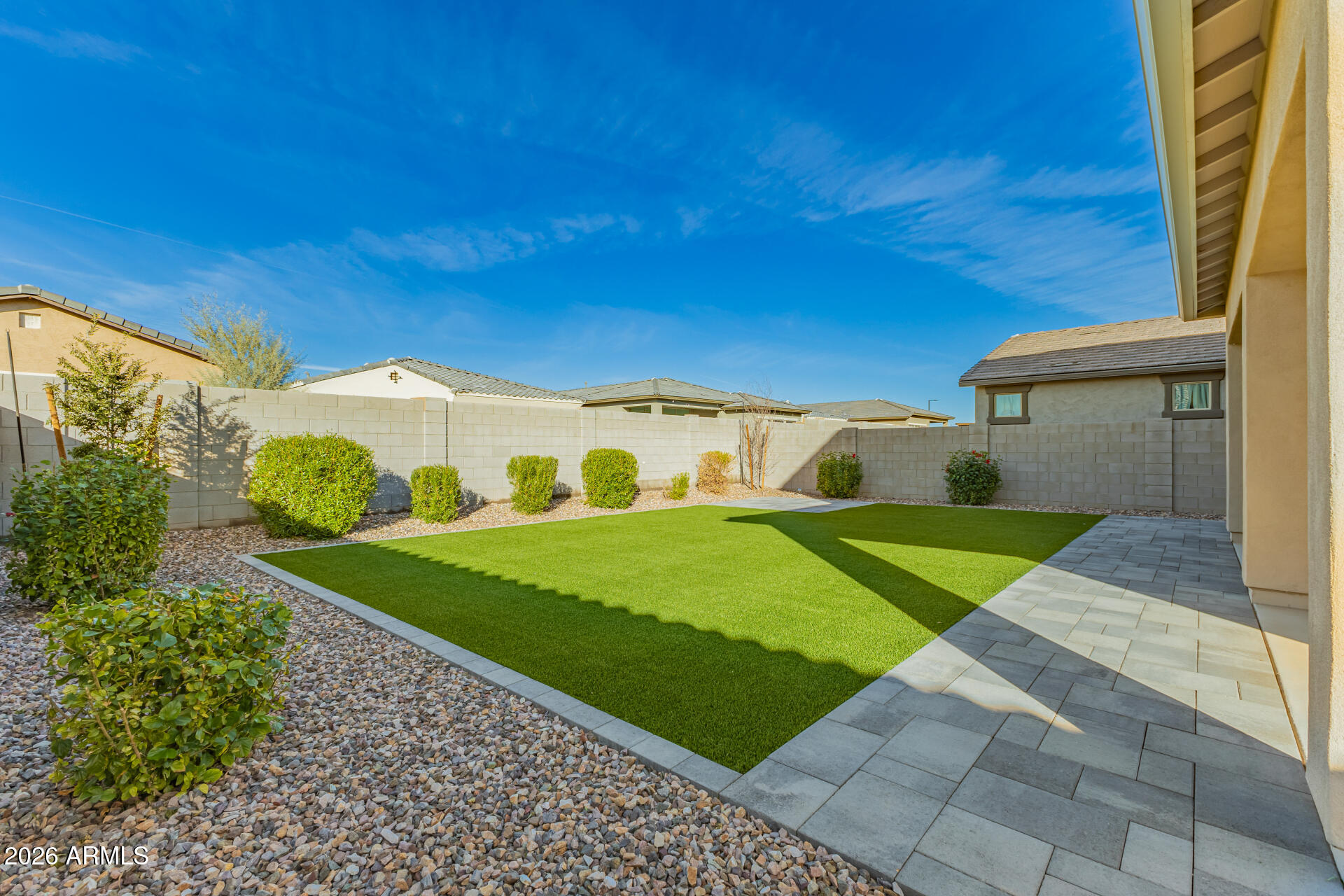 Backyard with a large artificial-turf lawn, gravel landscaping, and a paved patio.