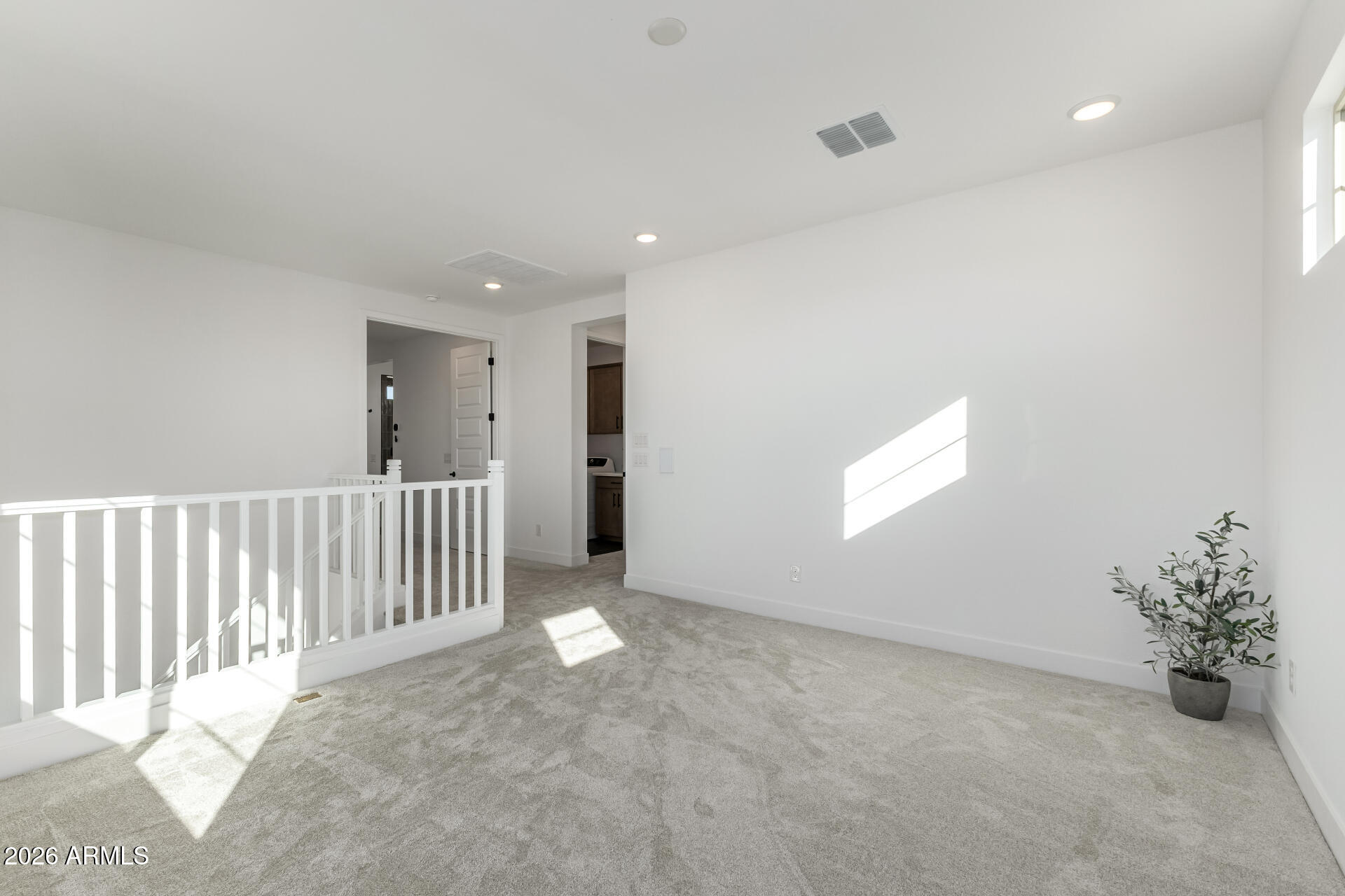 Carpeted upstairs landing with white stair railing, high window, and sunlight across the wall.