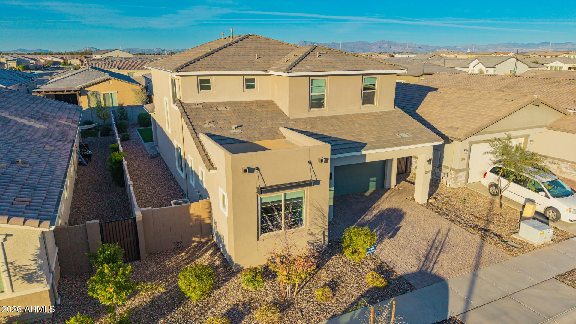 Aerial view of a two-story beige home with a paved driveway and mountain views.