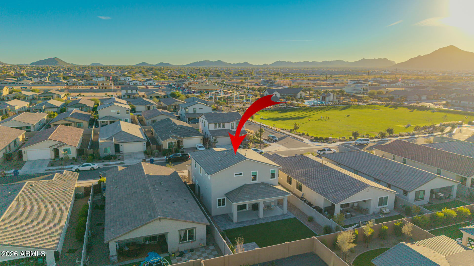 Aerial view of a two-story home beside a green park, marked by a red arrow, with mountains in the distance.