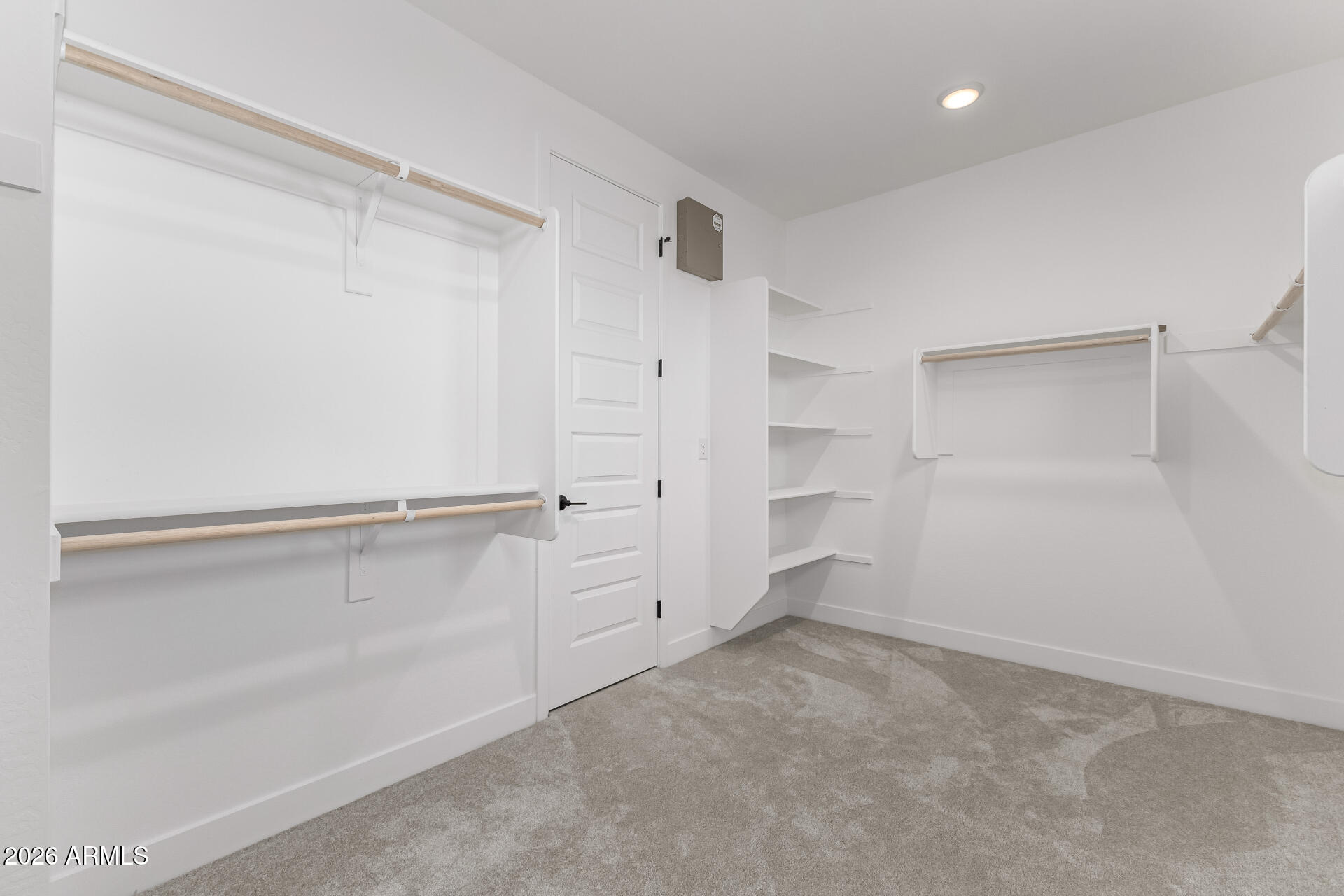 Walk-in closet with built-in shelves, multiple hanging rods, and gray carpet.