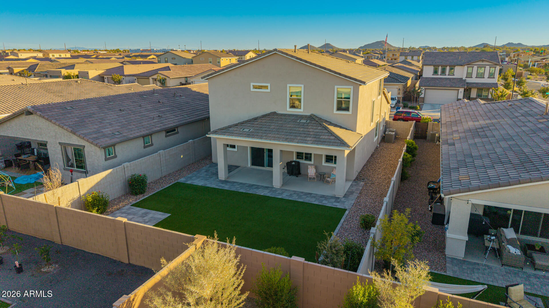 Aerial view of a two-story home and its walled backyard with a covered patio and green lawn.
