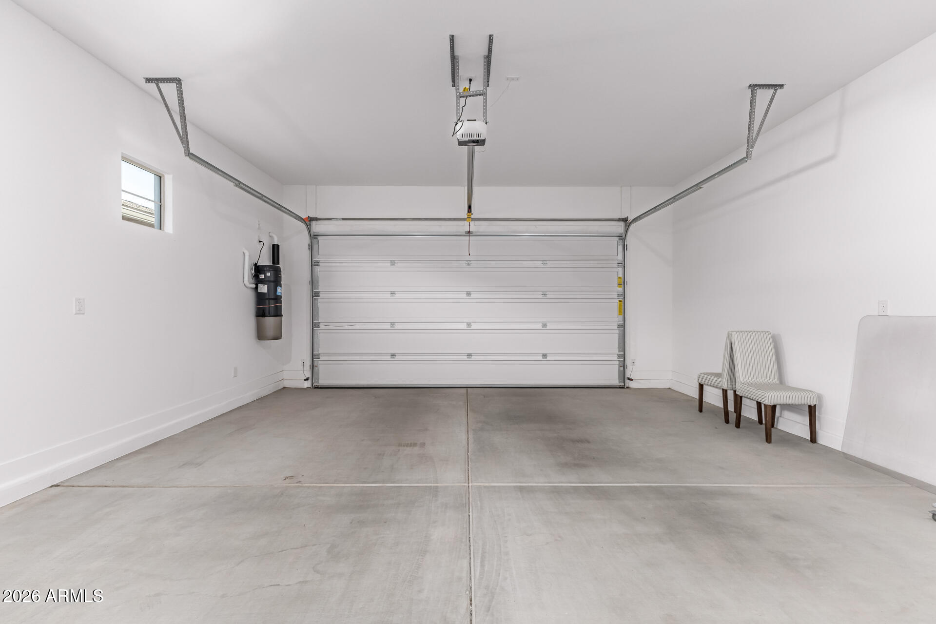 Two-car garage with a closed garage door, concrete floor, ceiling opener, and two chairs.