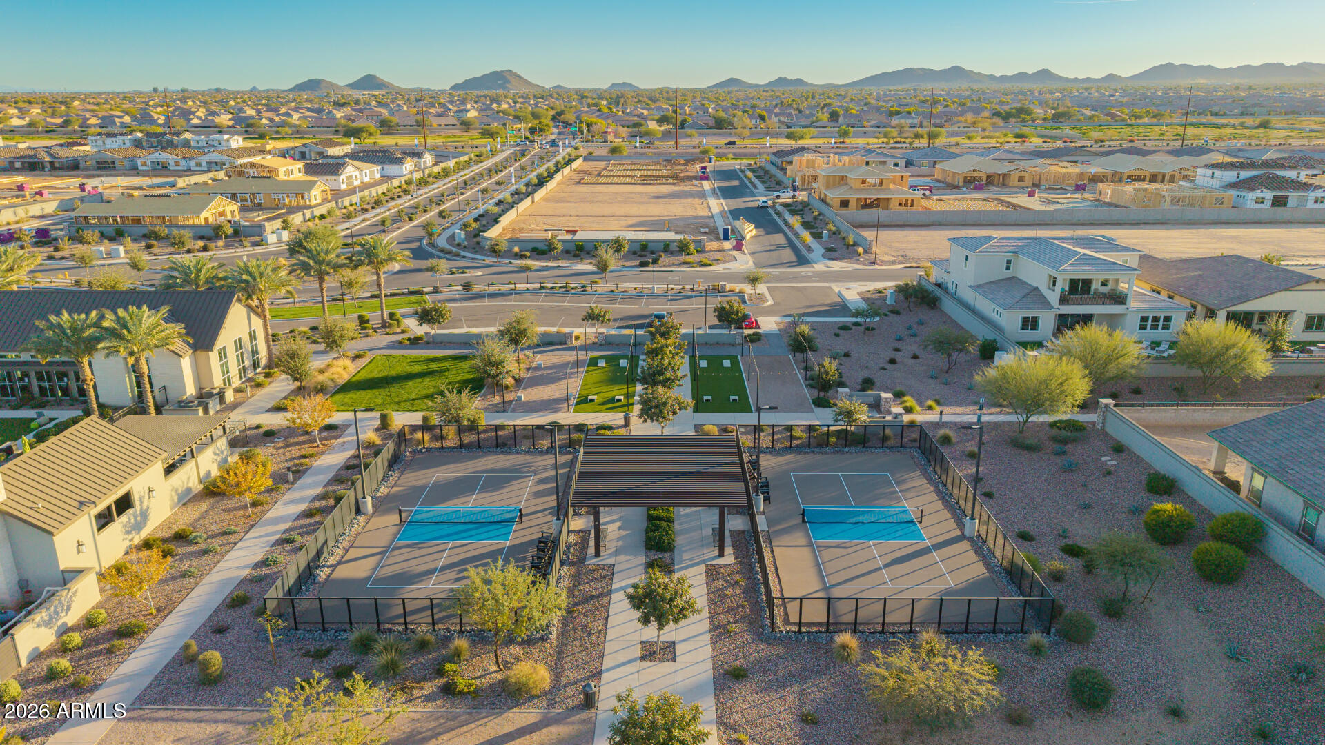 Aerial view of a community’s pickleball courts, desert landscaping, homes, and distant mountains.