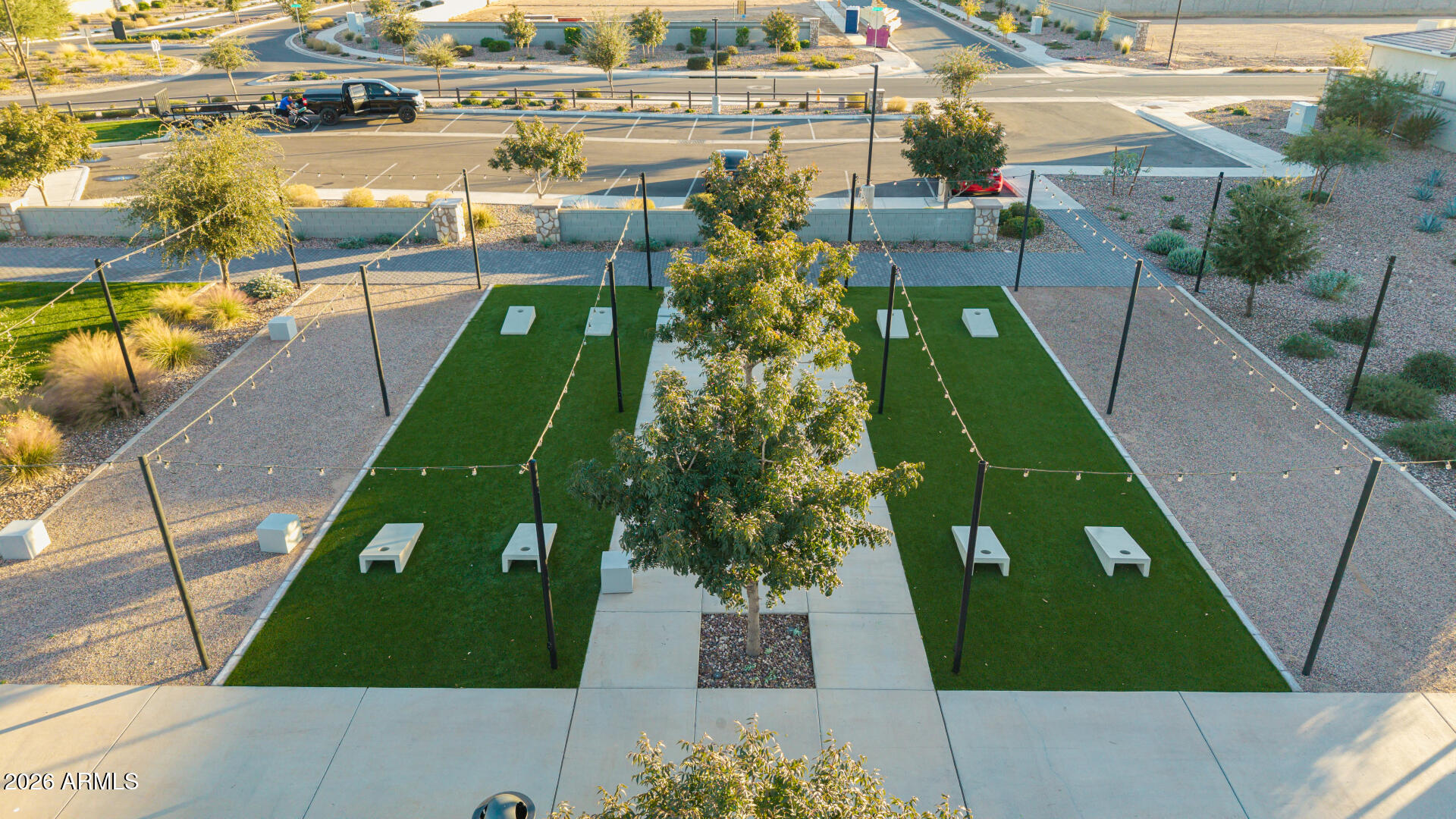 Aerial view of a landscaped community lawn with string lights and cornhole boards.