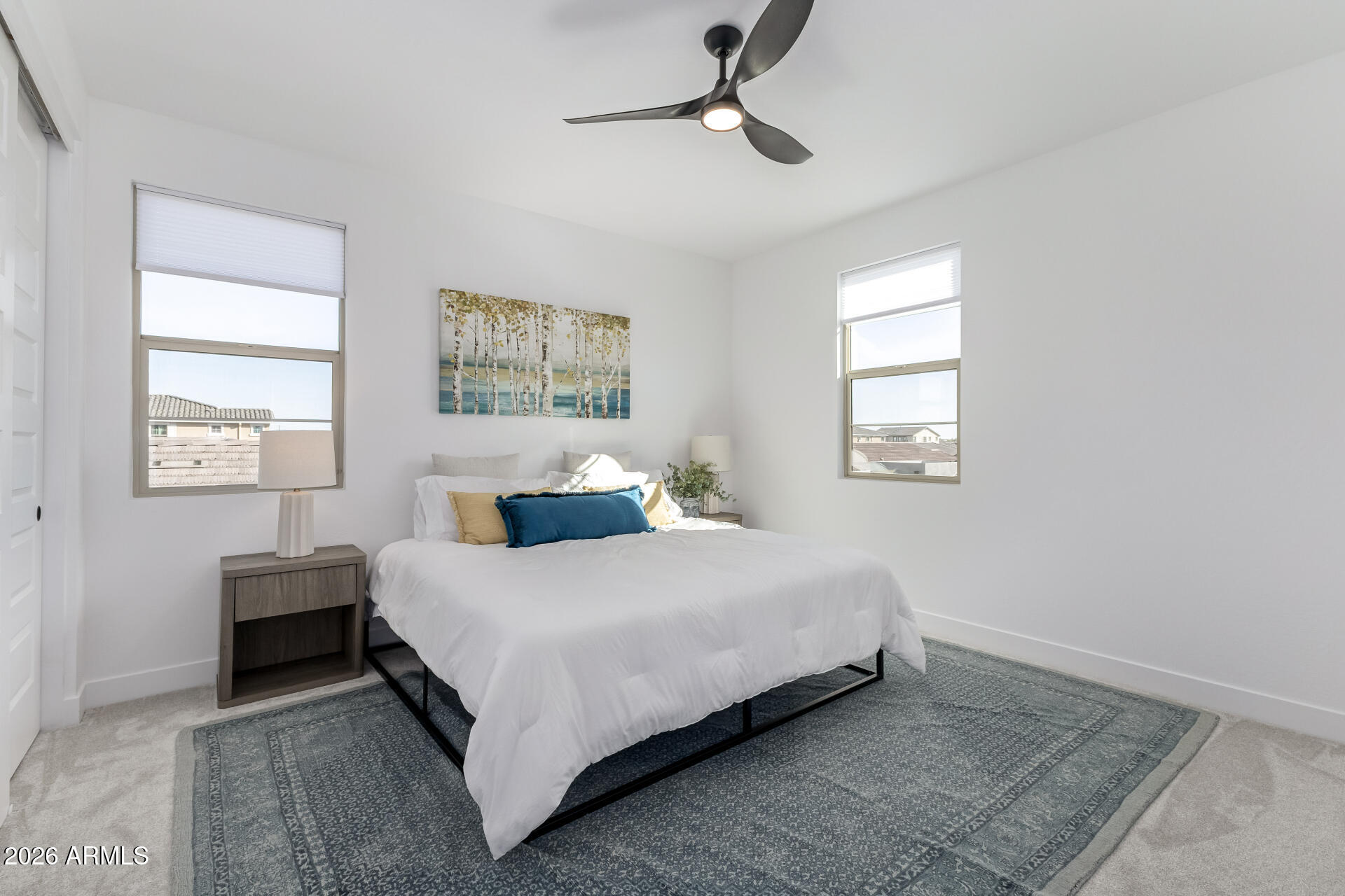 Furnished bedroom with a white bed, teal accent pillow, two windows, and a patterned rug.