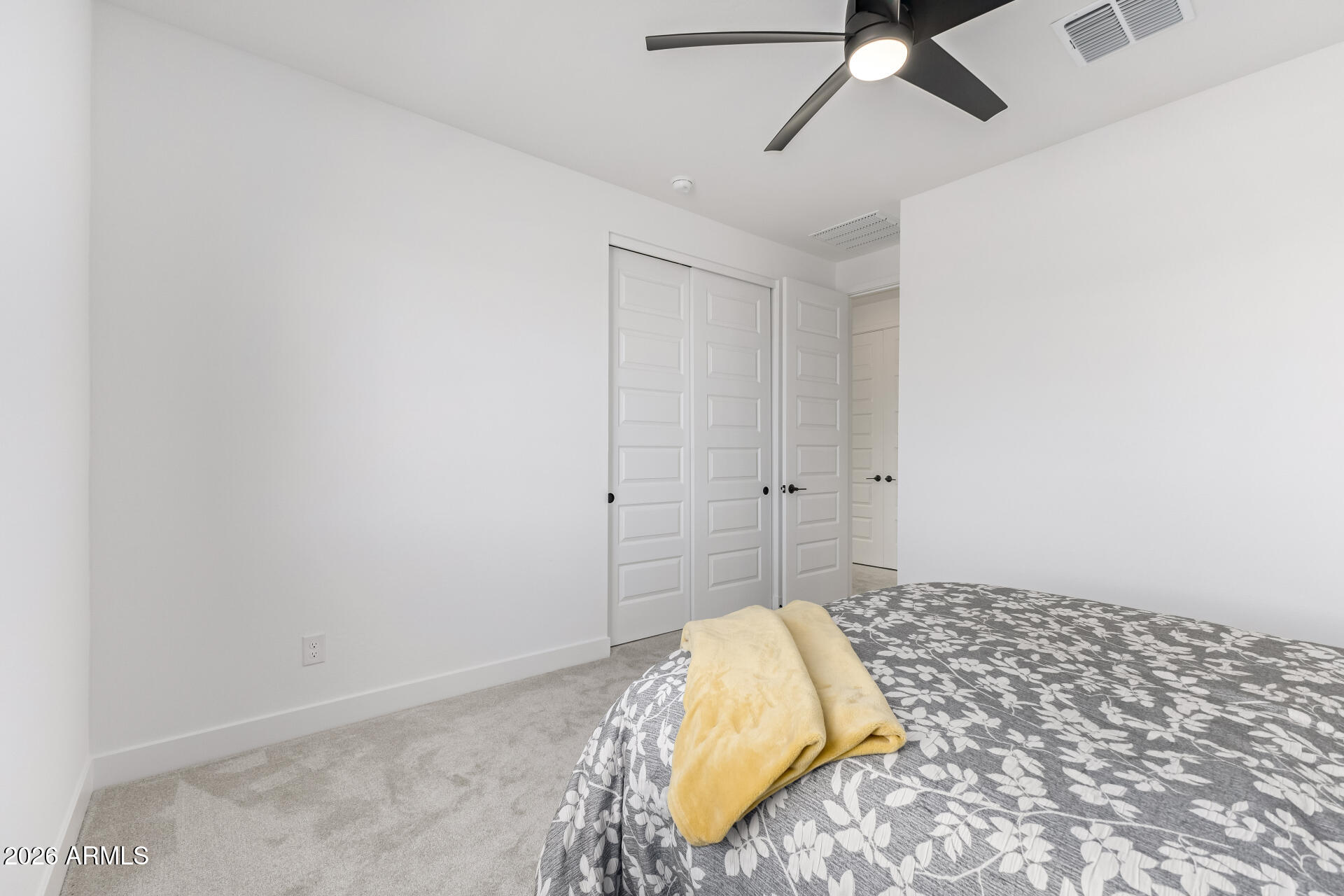 Bedroom with floral bedding, a yellow blanket, paneled closet doors, and a black ceiling fan.