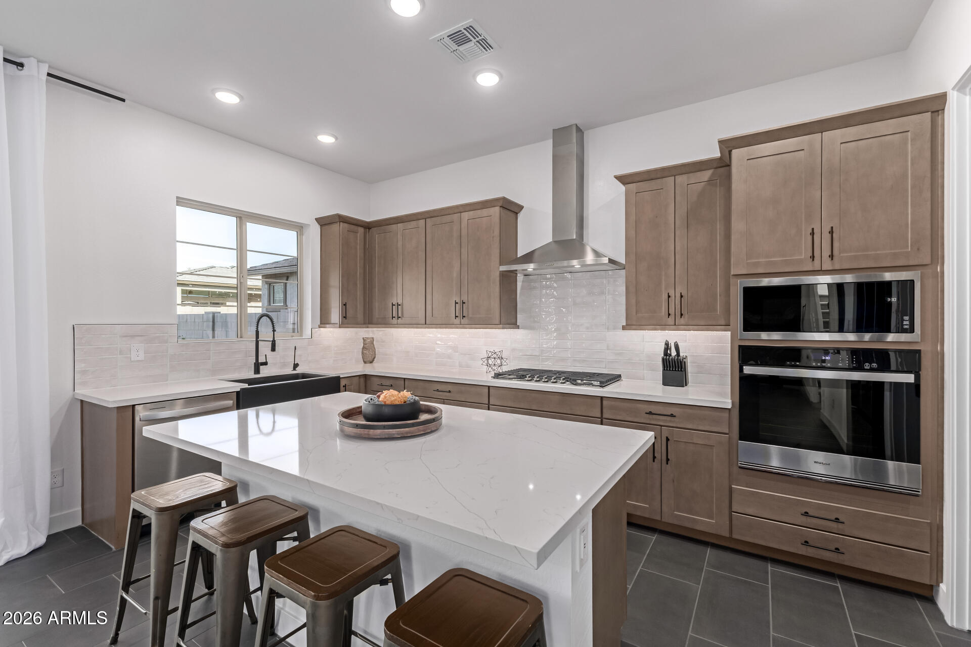 Kitchen with a large white island, taupe cabinets, and built-in stainless steel appliances.