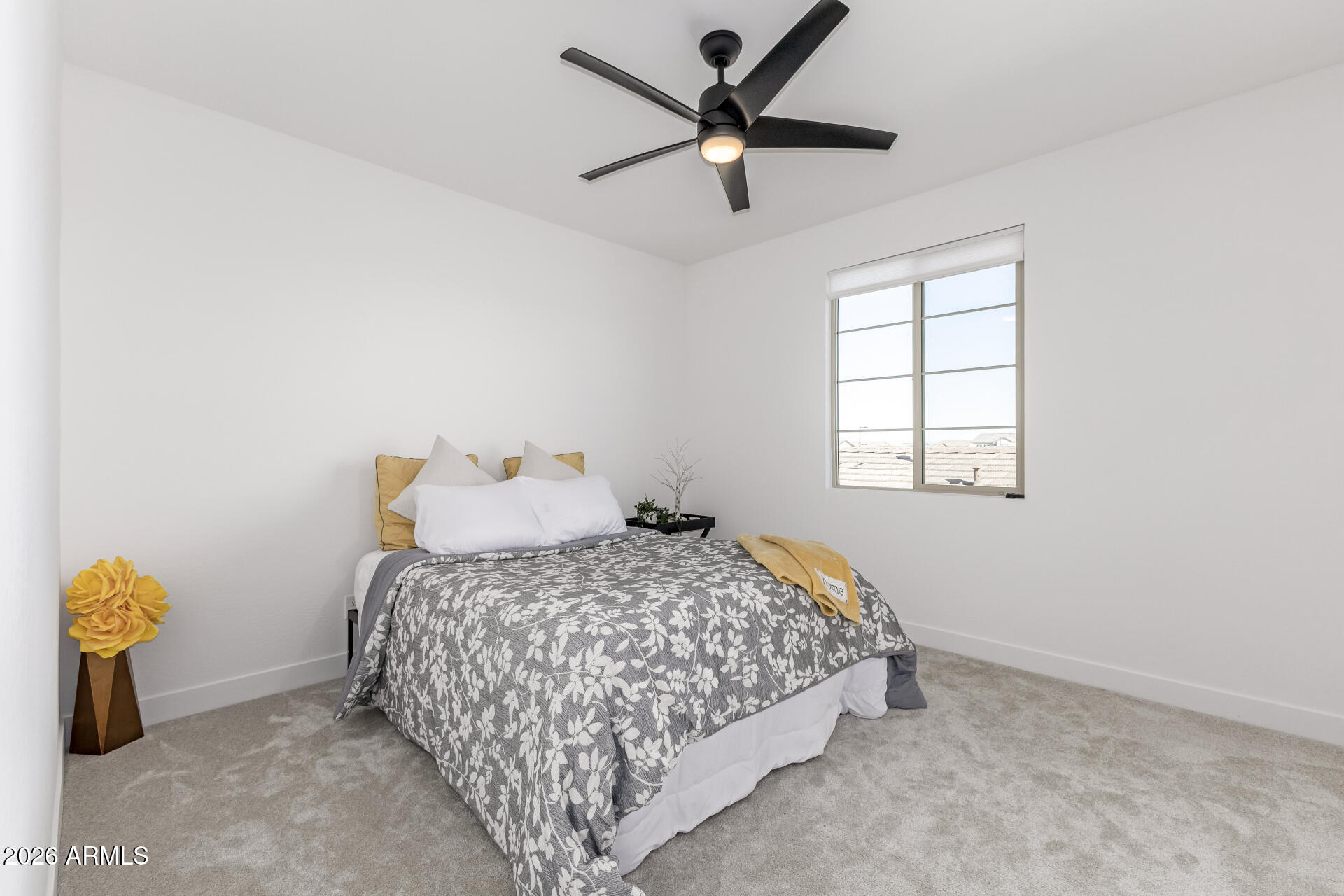 Staged bedroom with a floral bedspread, mustard-yellow accents, and a black ceiling fan.