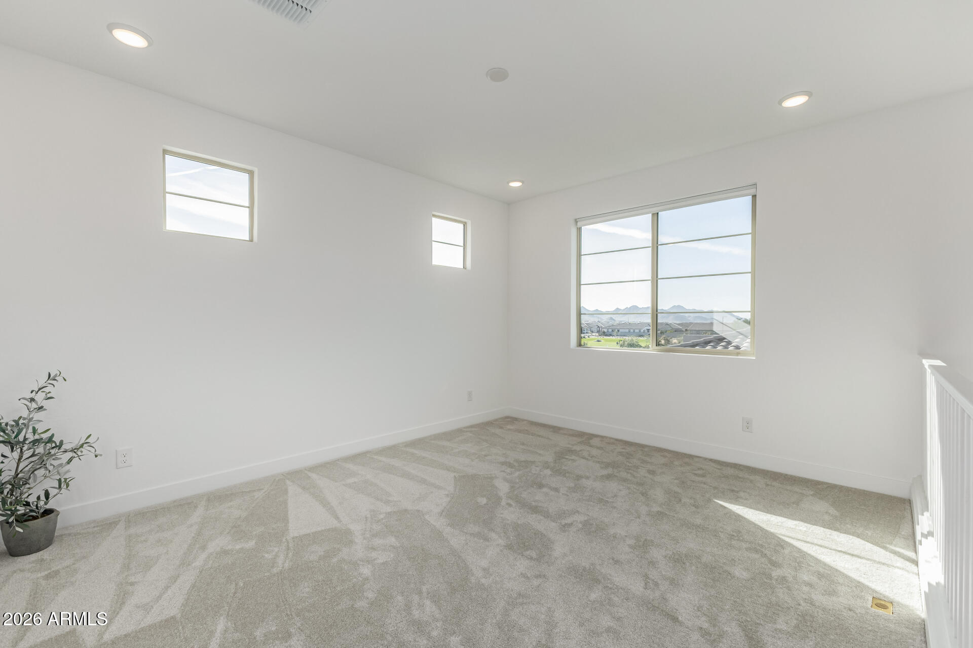 Vacant upstairs room with gray carpet, multiple windows, and a view of distant mountains.
