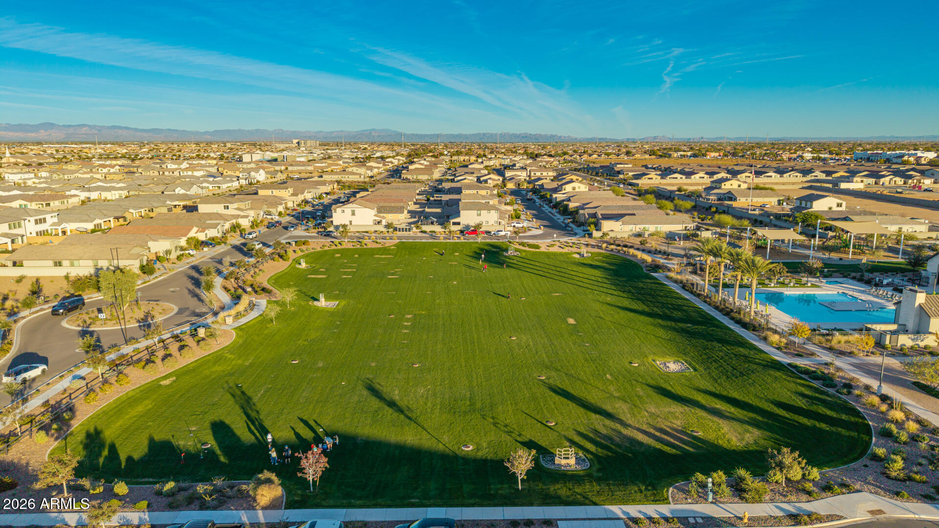Aerial view of a residential community with a large green park, swimming pool, and distant mountains.