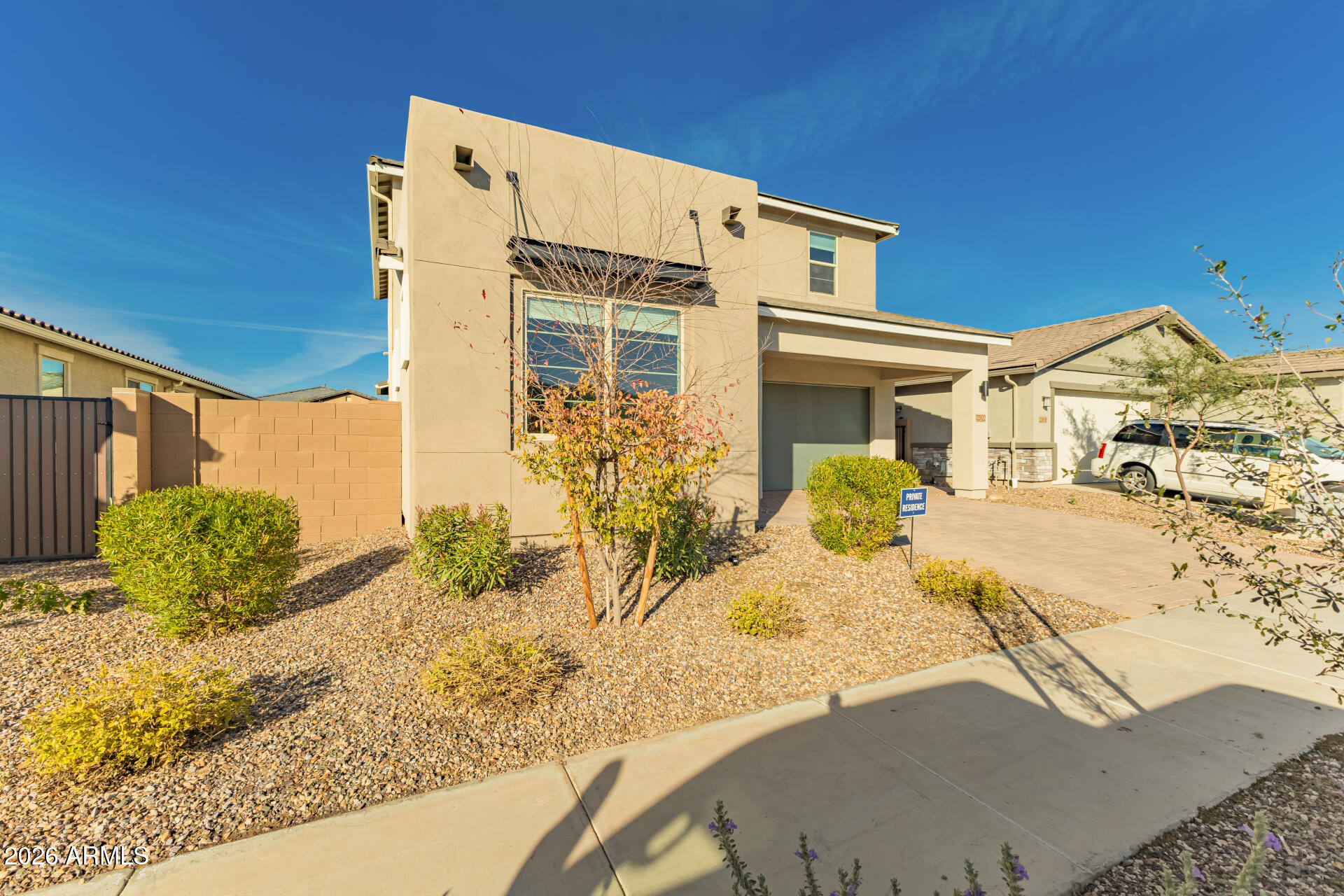 Two-story beige stucco home with a covered entry, paved driveway, and gravel landscaping.