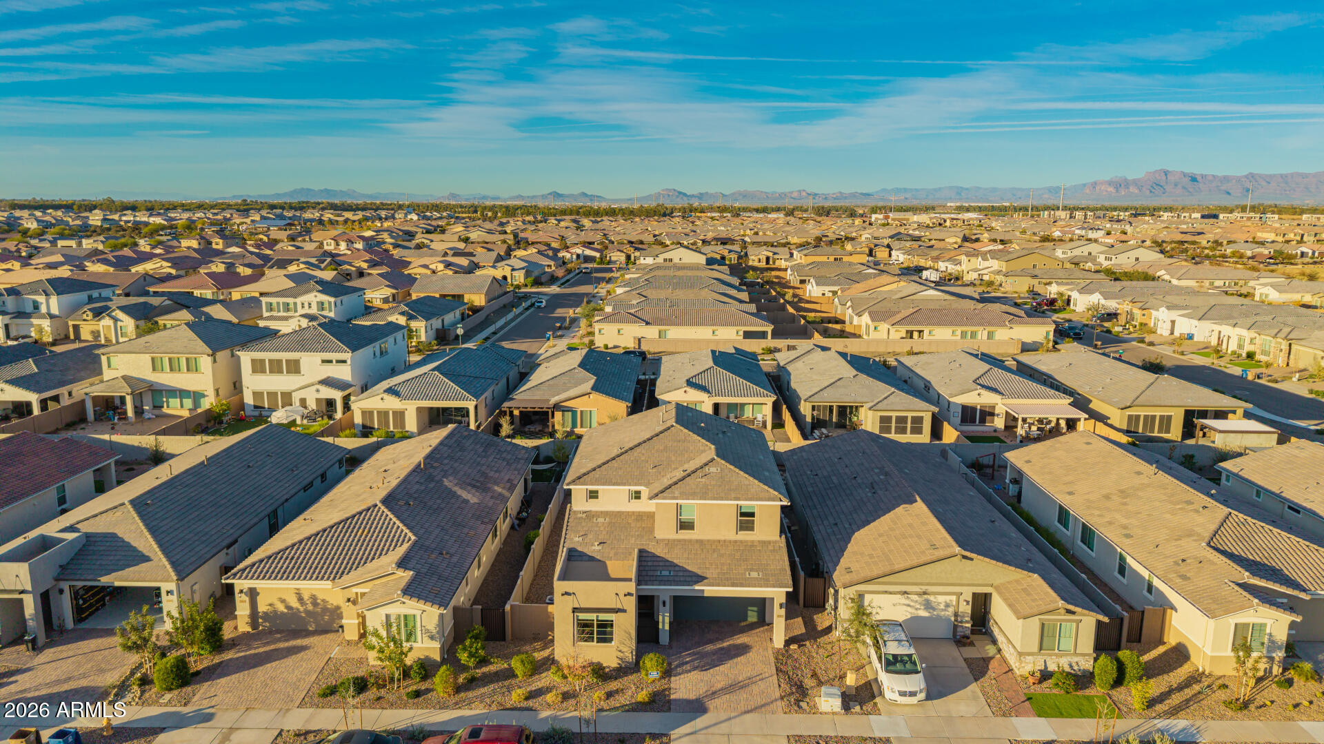 Aerial view of a Queen Creek home among a dense neighborhood, with mountains on the horizon.