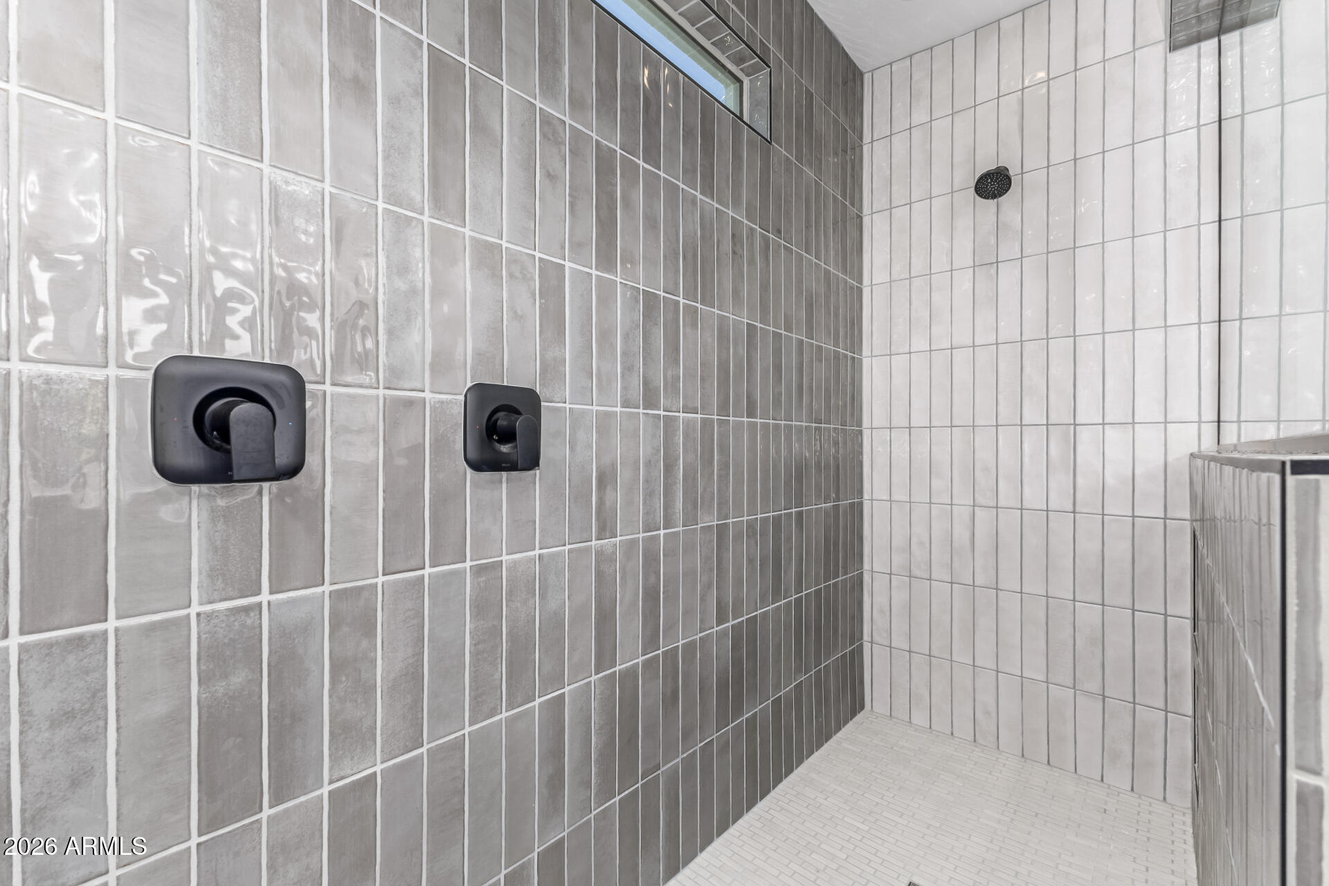 Walk-in shower with gray and white tile, black fixtures, and a small high window.