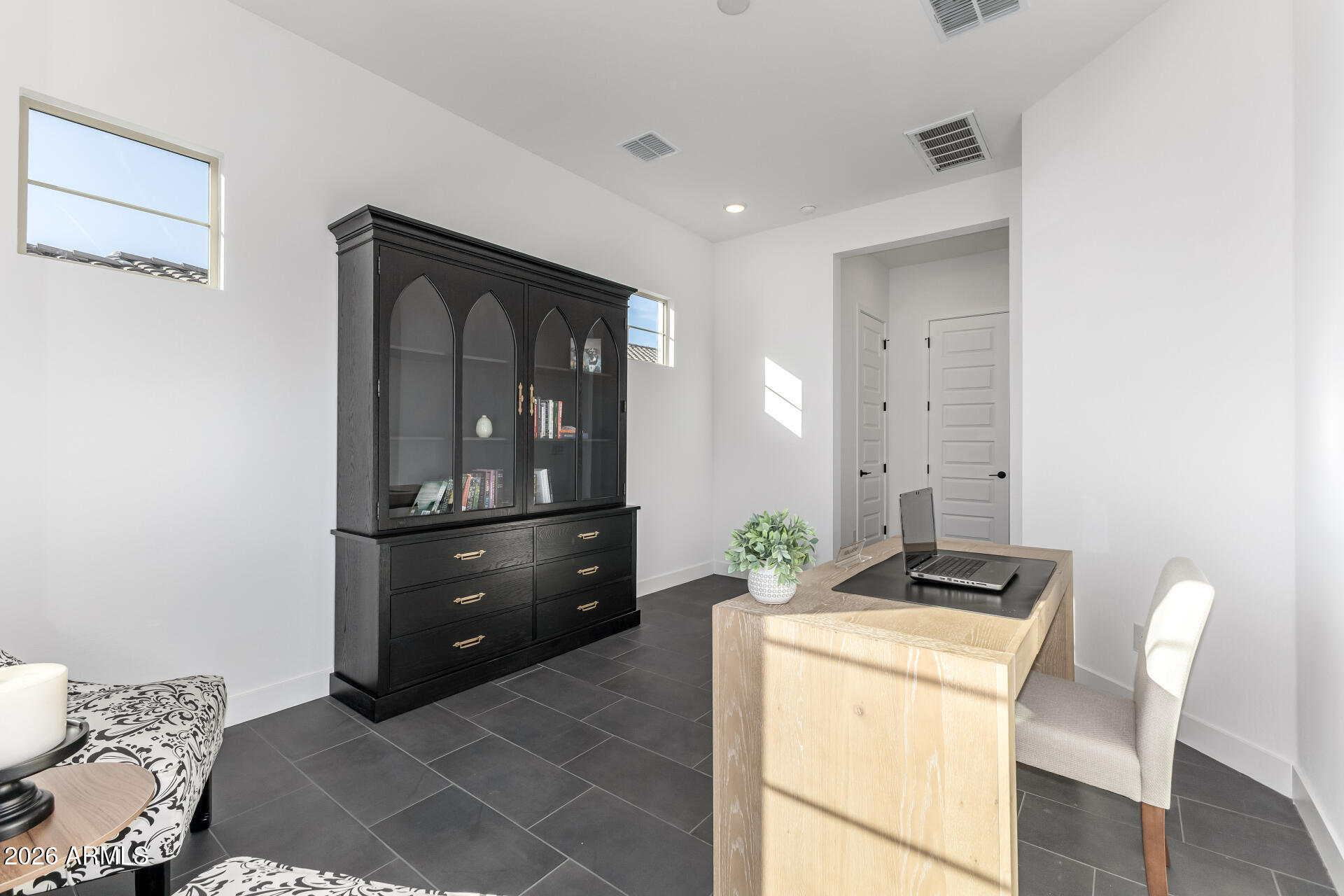 Furnished home office with a light wood desk, laptop, and large black glass-front cabinet.