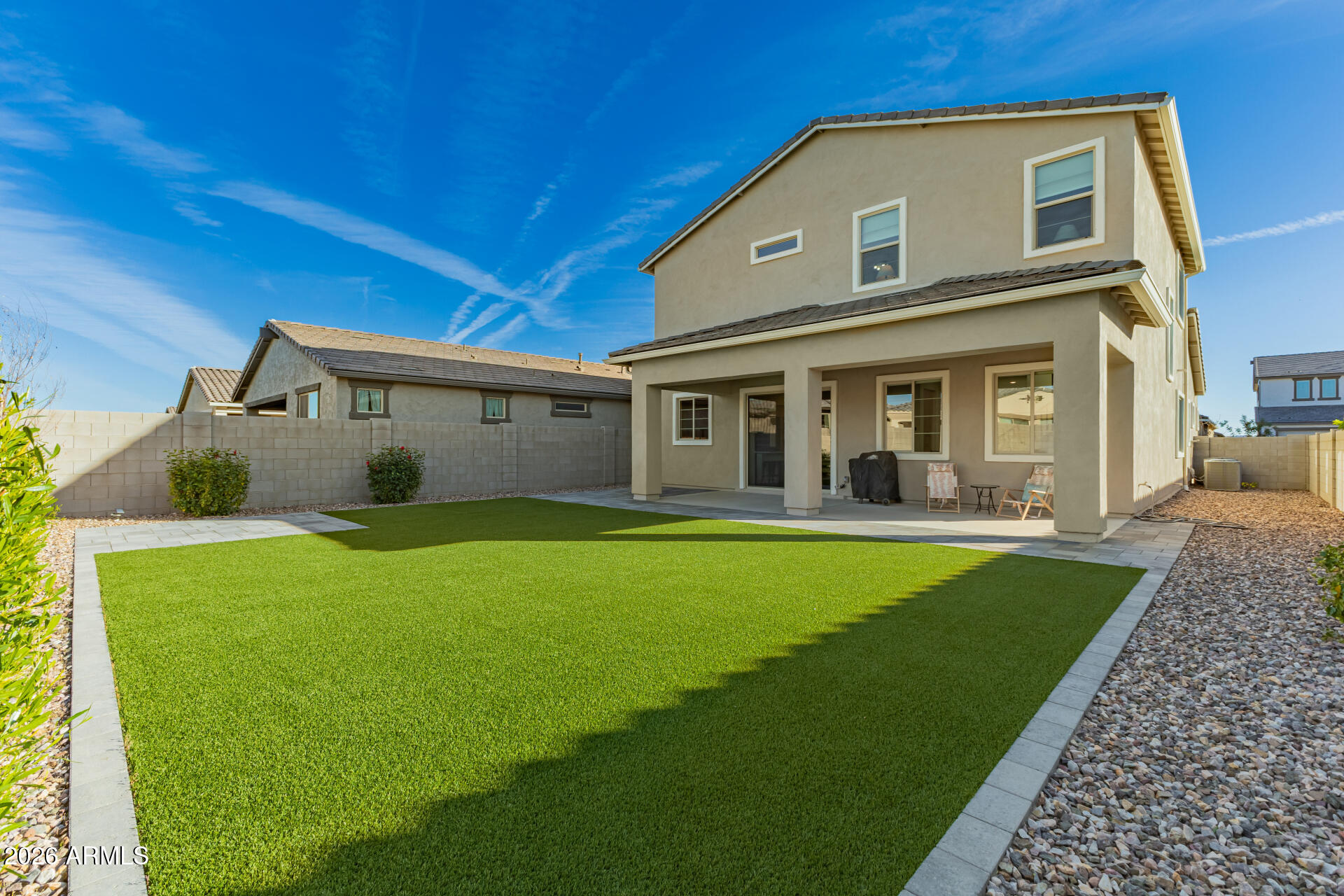 Two-story home's backyard with covered patio, artificial turf lawn, and gravel landscaping.