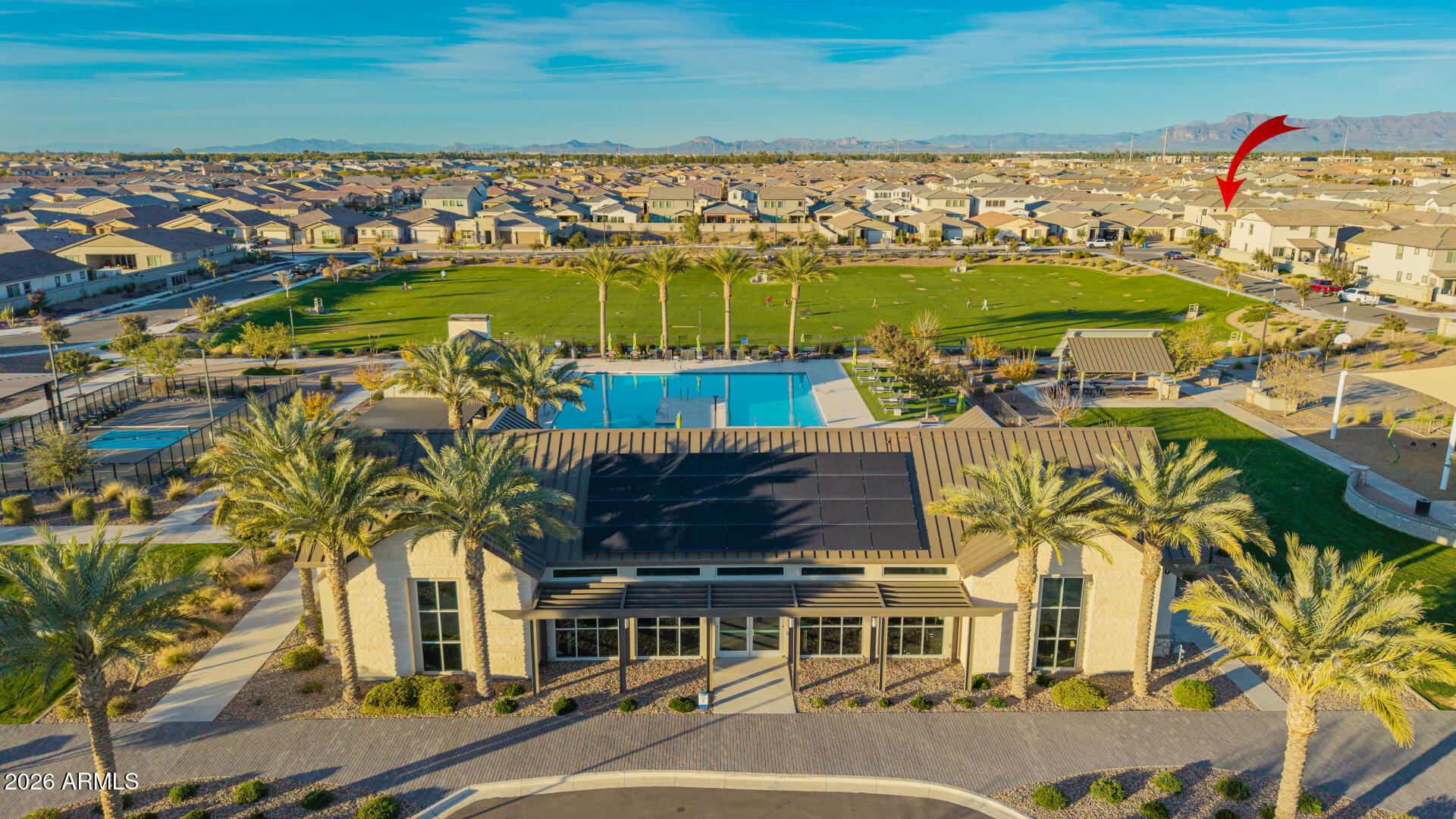 Aerial view of the marked neighborhood home, with a clubhouse, pool, park, and mountains nearby.