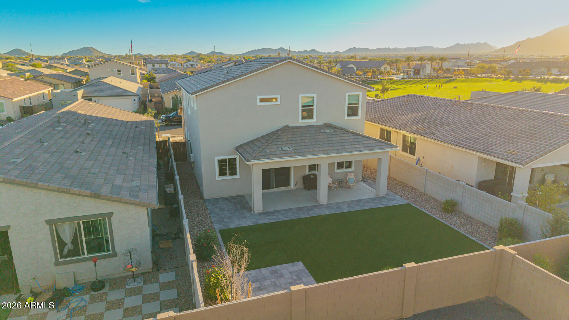 Aerial view of a two-story home’s backyard with a covered patio, artificial lawn, and distant mountains.