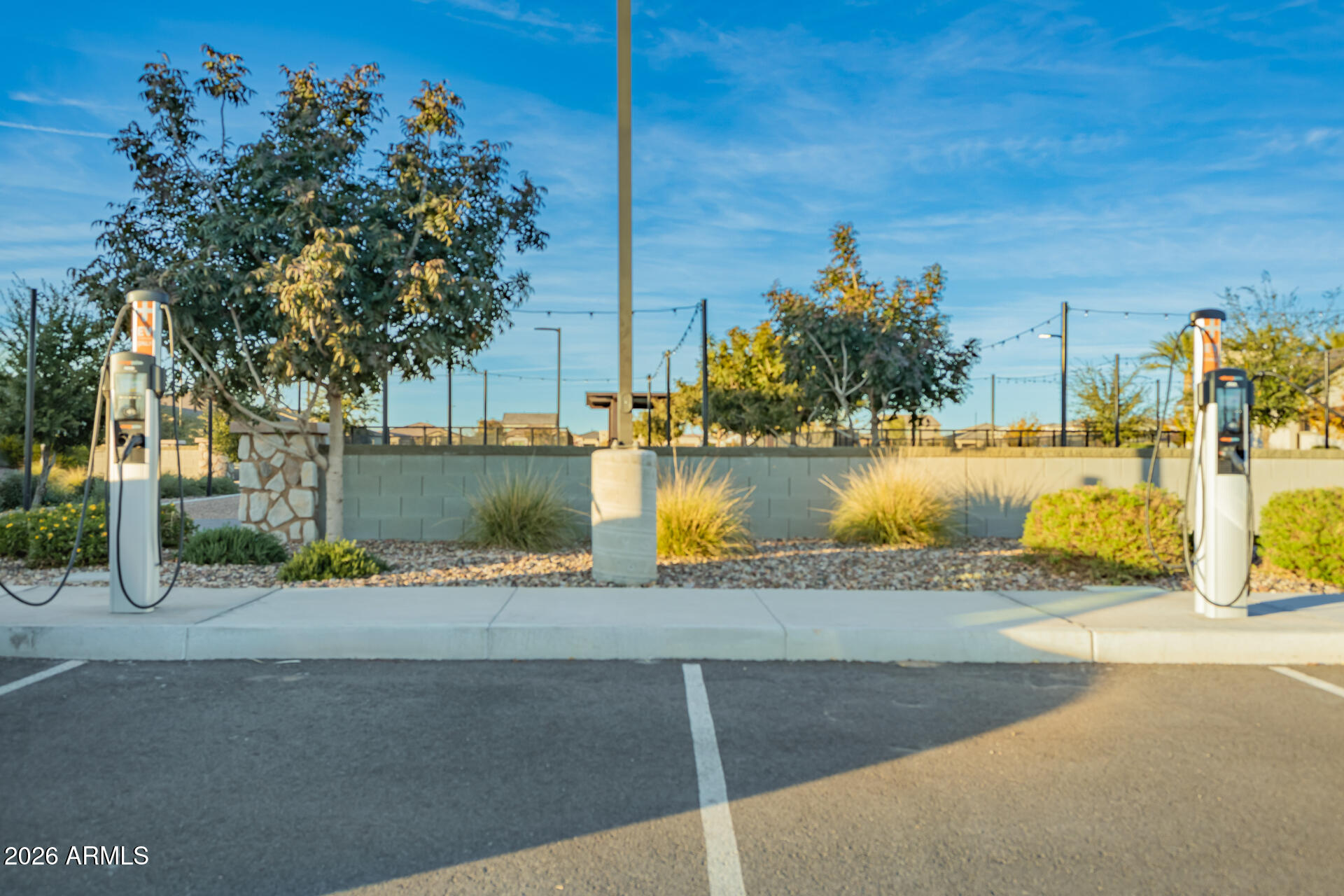 Two electric vehicle charging stations beside a landscaped parking area and fenced recreation area.