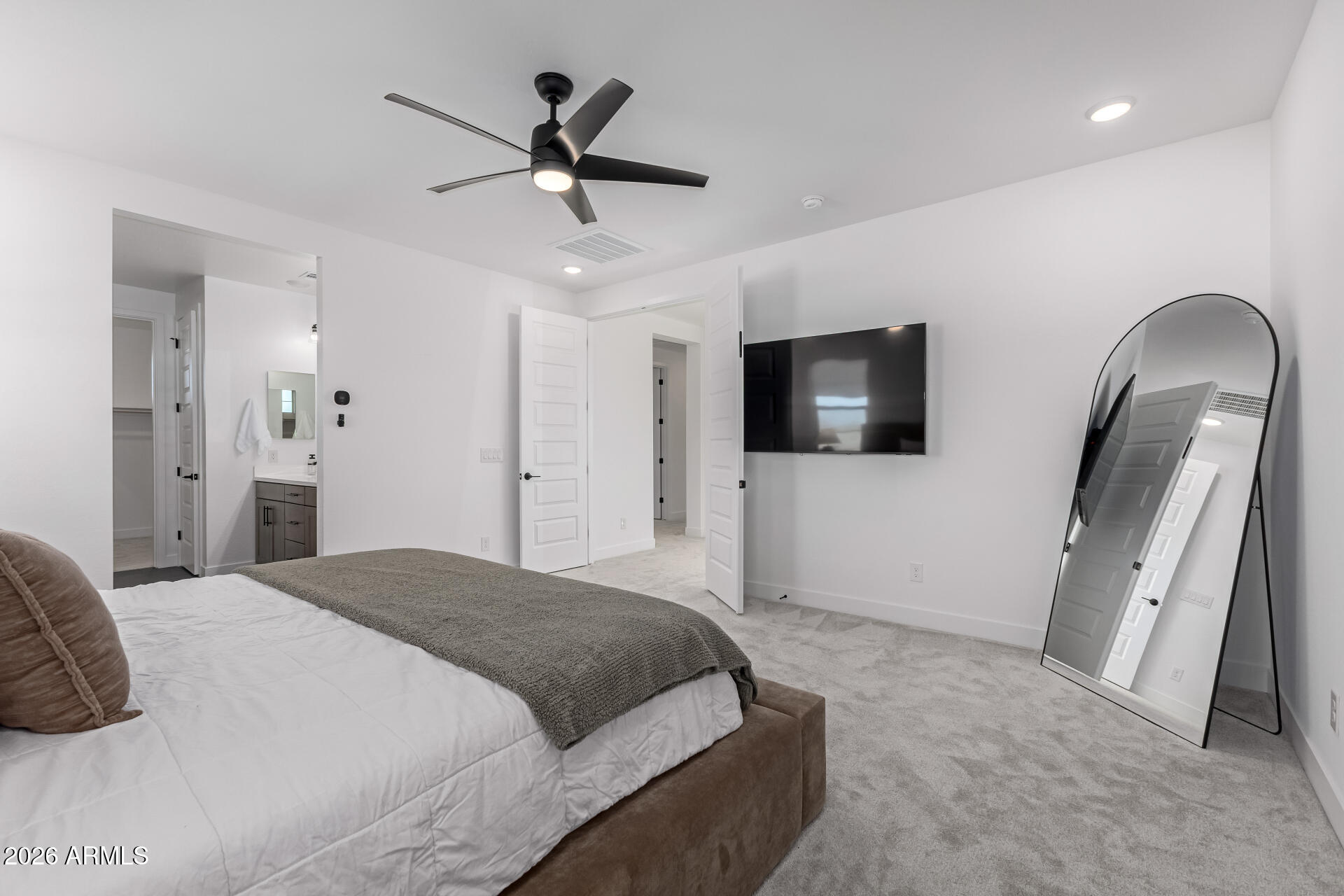 Bedroom with a gray-covered bed, wall-mounted TV, black ceiling fan, and tall arched mirror.
