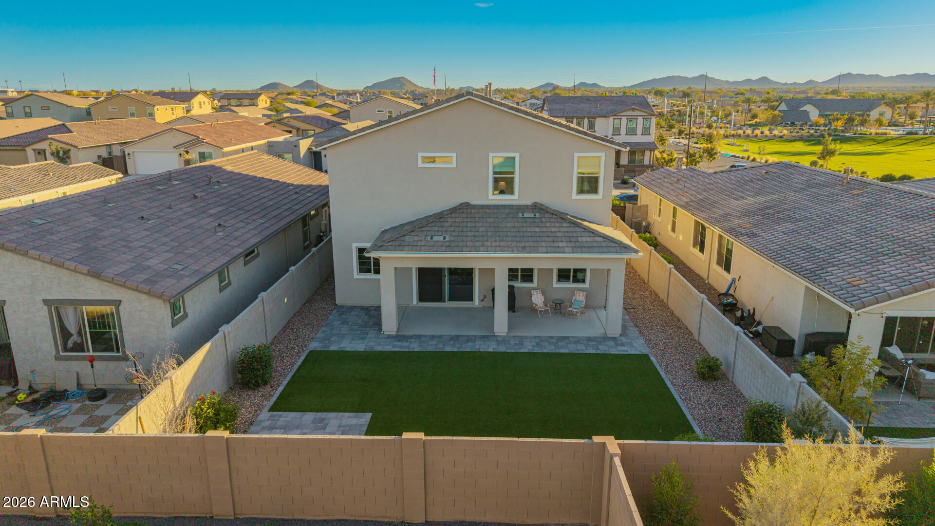 Aerial view of a home’s rear yard with a covered patio, lawn, and distant mountains.