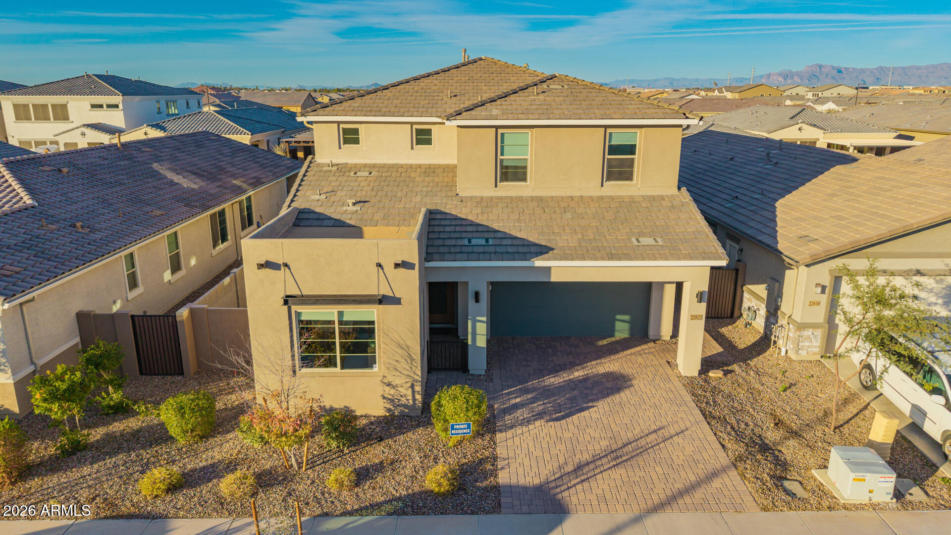 Two-story beige stucco home with a tiled roof, two-car garage, and gravel landscaping, seen from above.