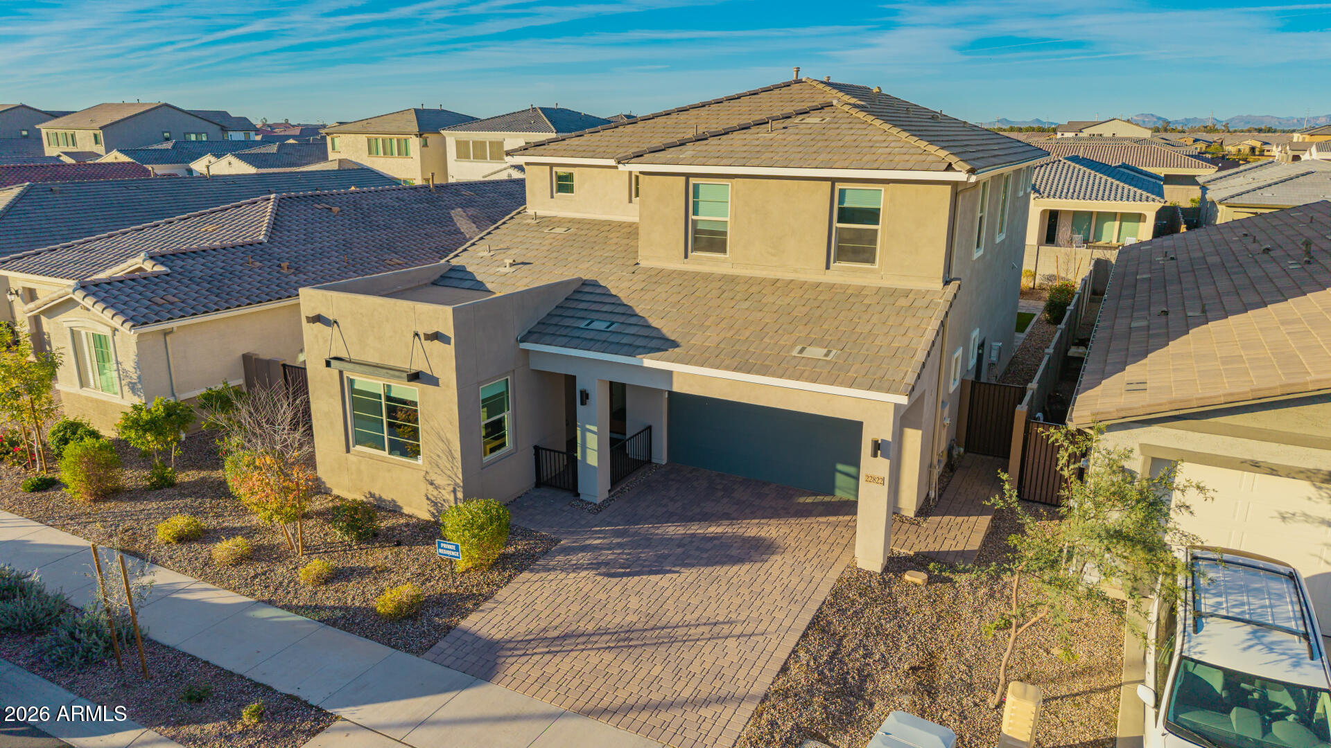 Two-story beige stucco home with a tile roof, double garage, and paver driveway, viewed from above.