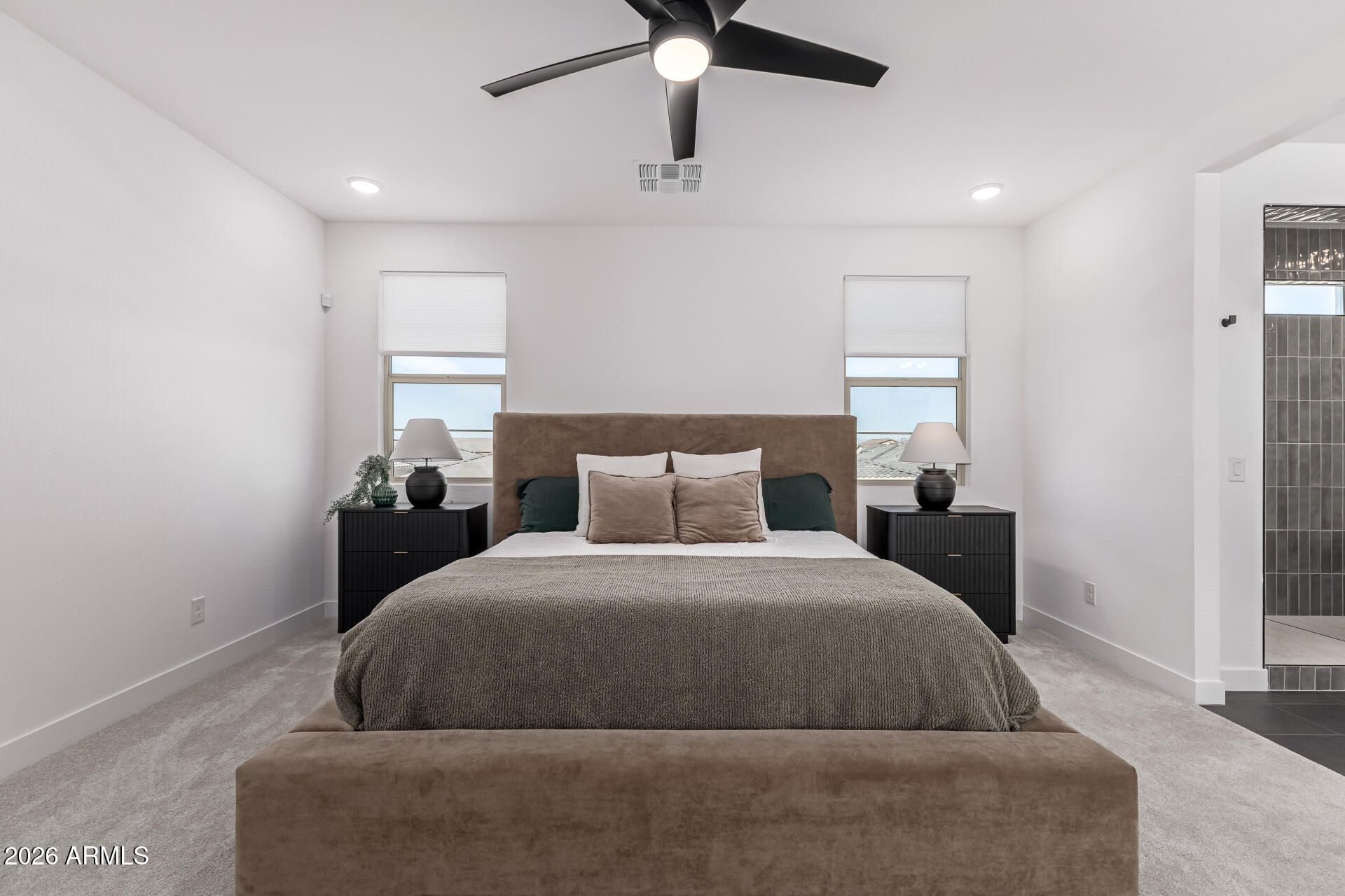 Staged bedroom with a centered bed, matching nightstands, two windows, and a ceiling fan.