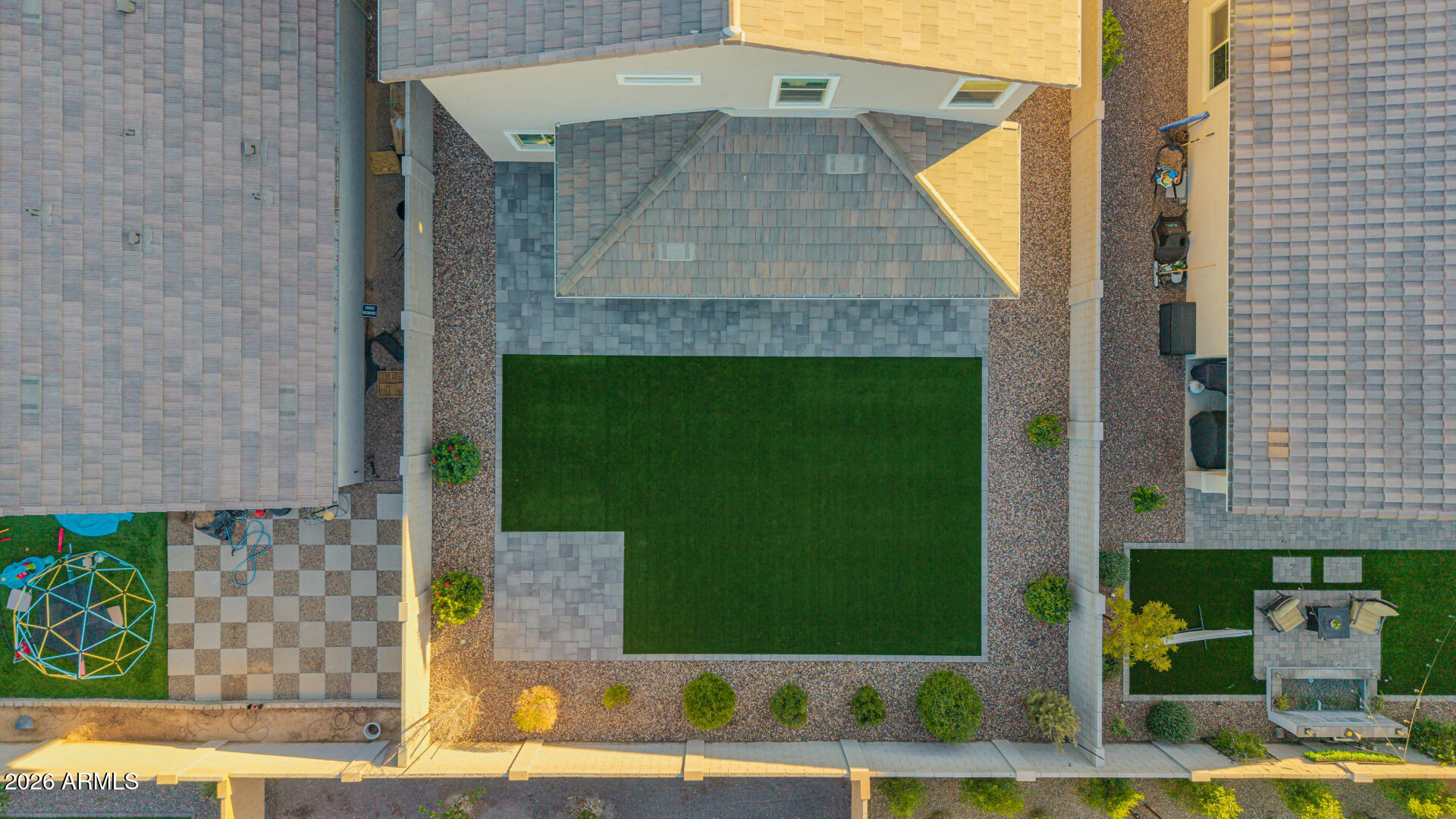 Backyard with a large lawn, checkerboard paver patio, children's climbing dome, and outdoor seating area.