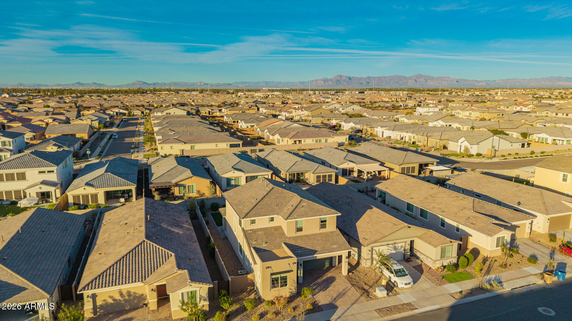 Aerial view of a suburban neighborhood with rows of tiled-roof homes and distant mountains.