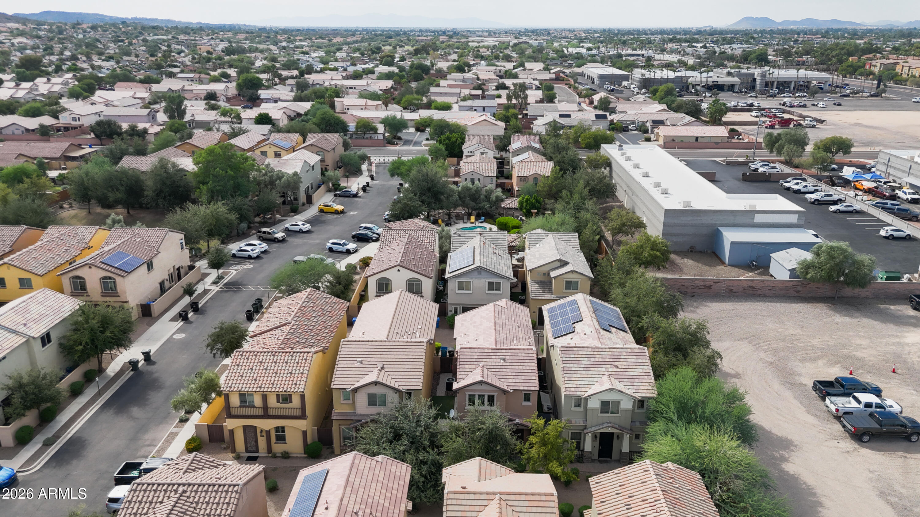 Aerial view of tile-roofed homes with solar panels, a commercial building, and distant mountains.