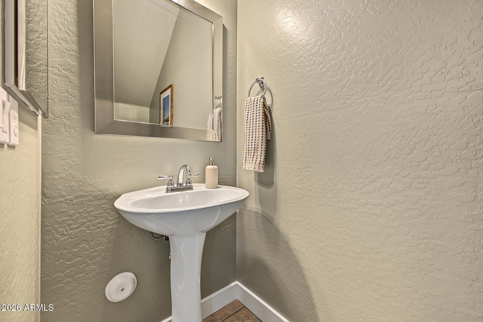 Bathroom pedestal sink with chrome faucet, framed mirror, and patterned hand towel.