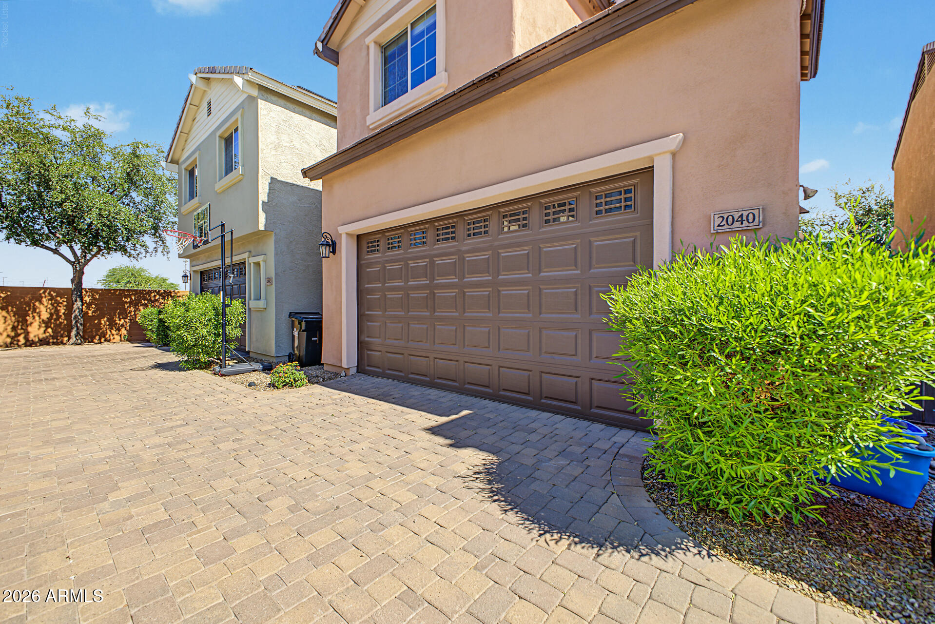 Two-story stucco home with a wide garage, paver driveway, and basketball hoop.
