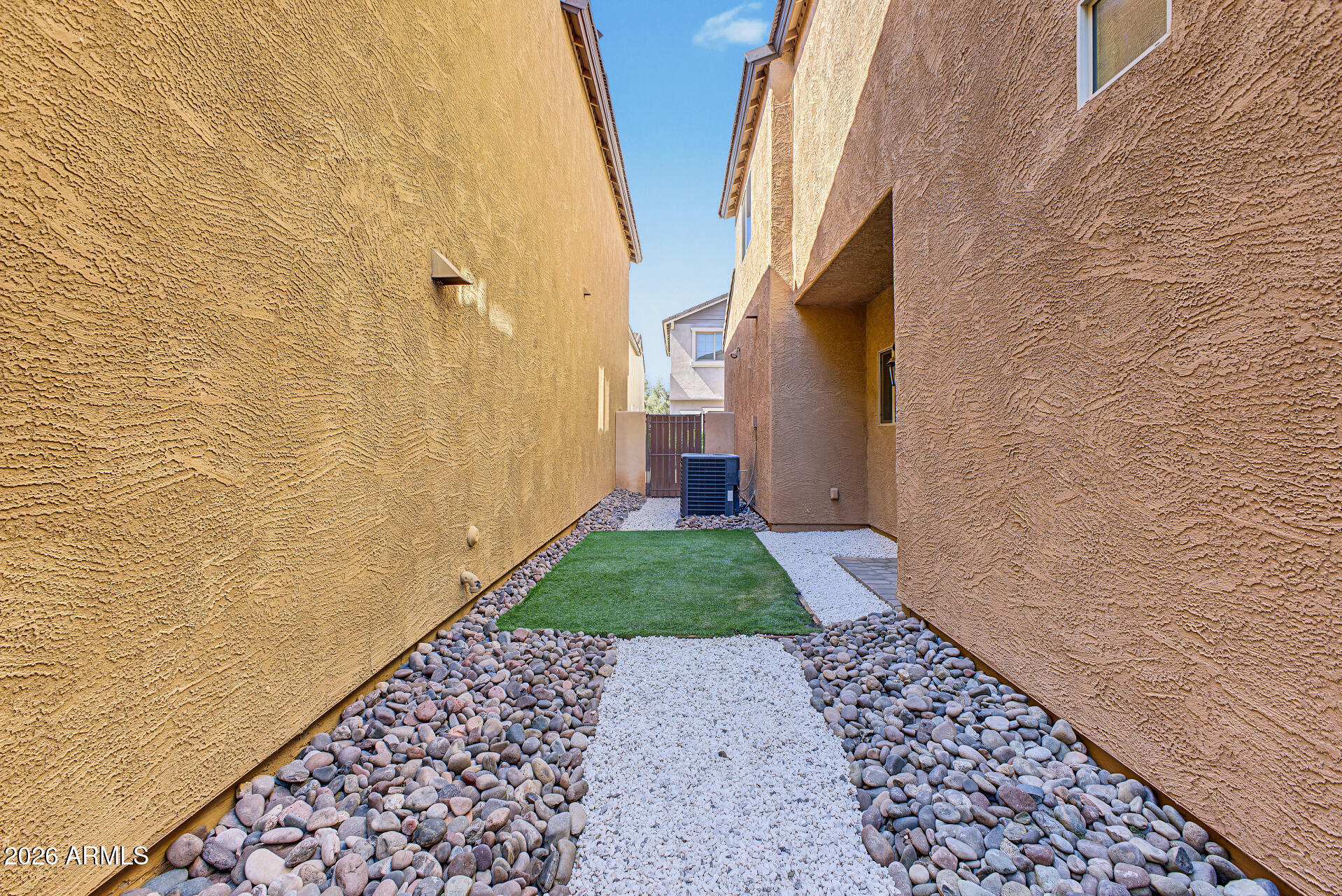 Narrow side yard with artificial turf, white gravel, river rocks, and an air-conditioning unit.
