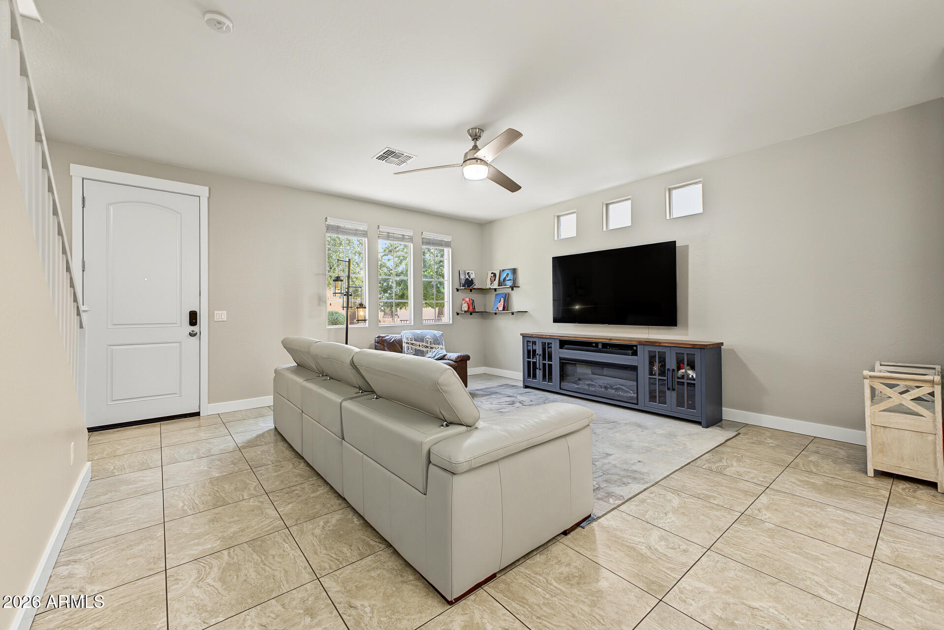 Furnished living room with a light sectional, tiled floors, and wall-mounted television.