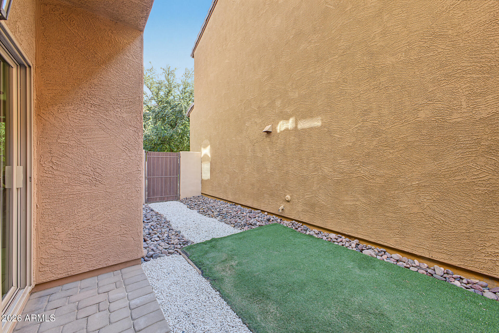 Enclosed side yard with artificial turf, gravel paths, river rocks, and a metal gate.