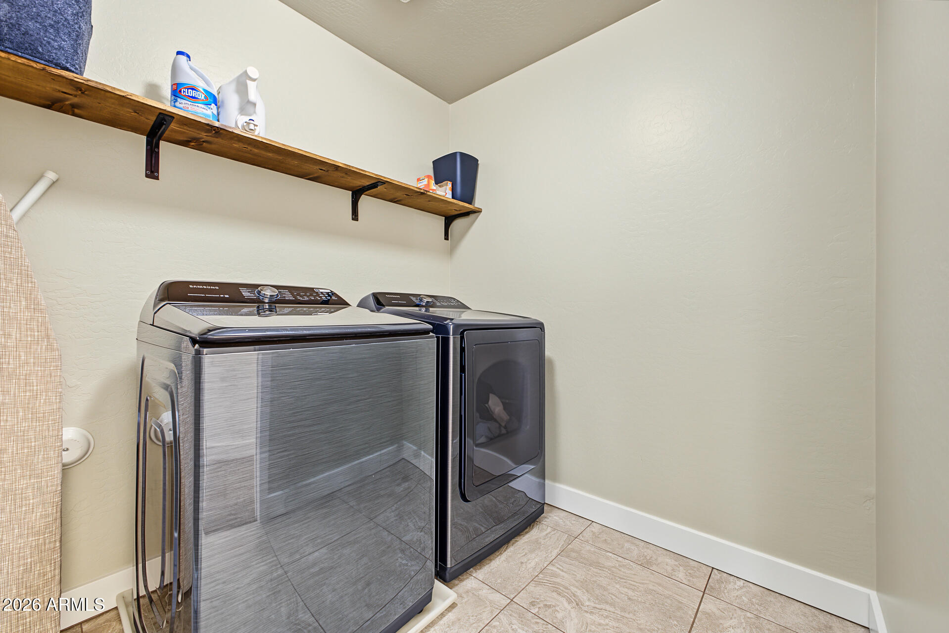 Laundry room with matching washer and dryer beneath a long wooden shelf.