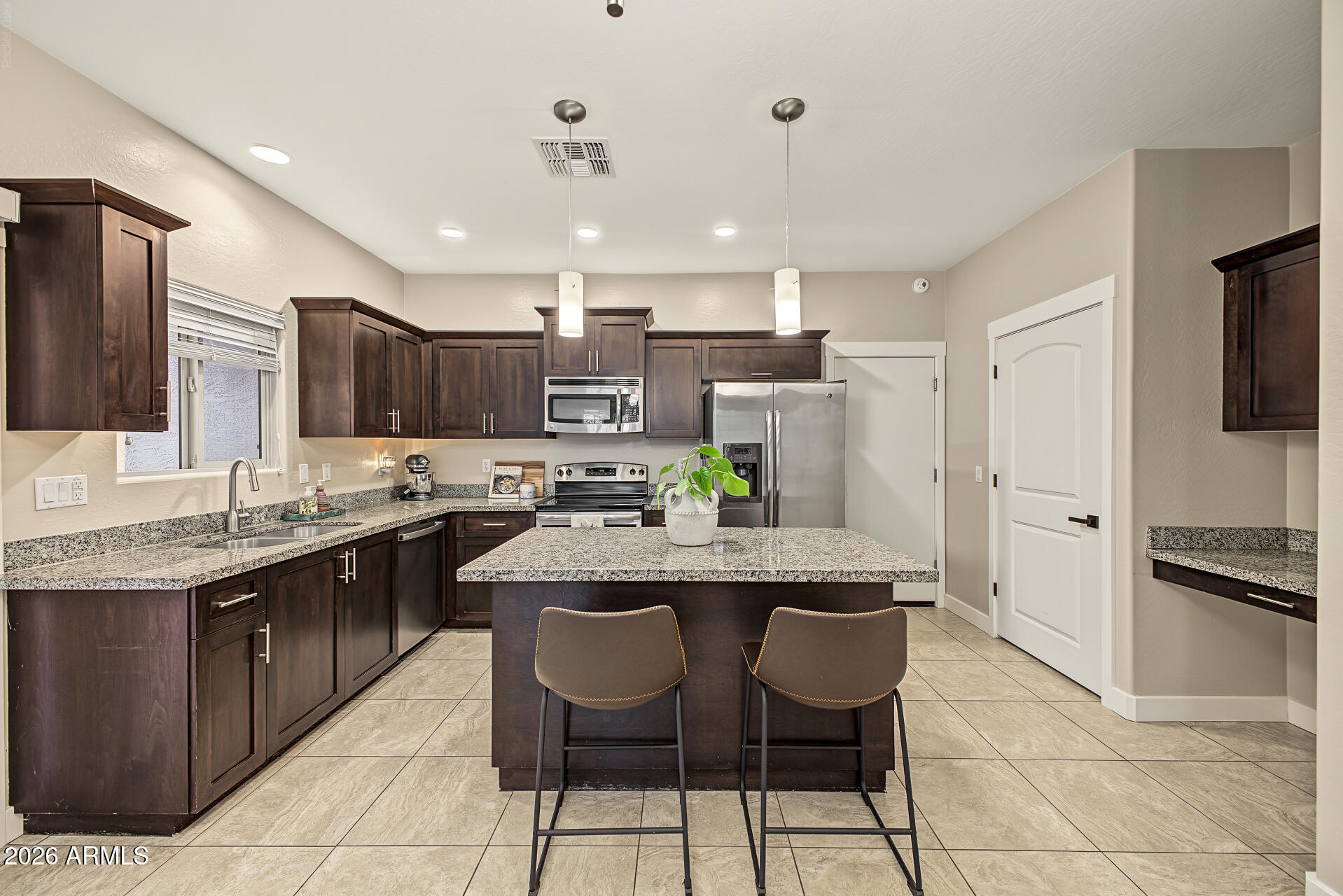 Kitchen with dark wood cabinets, granite island, stainless steel appliances, and two stools.