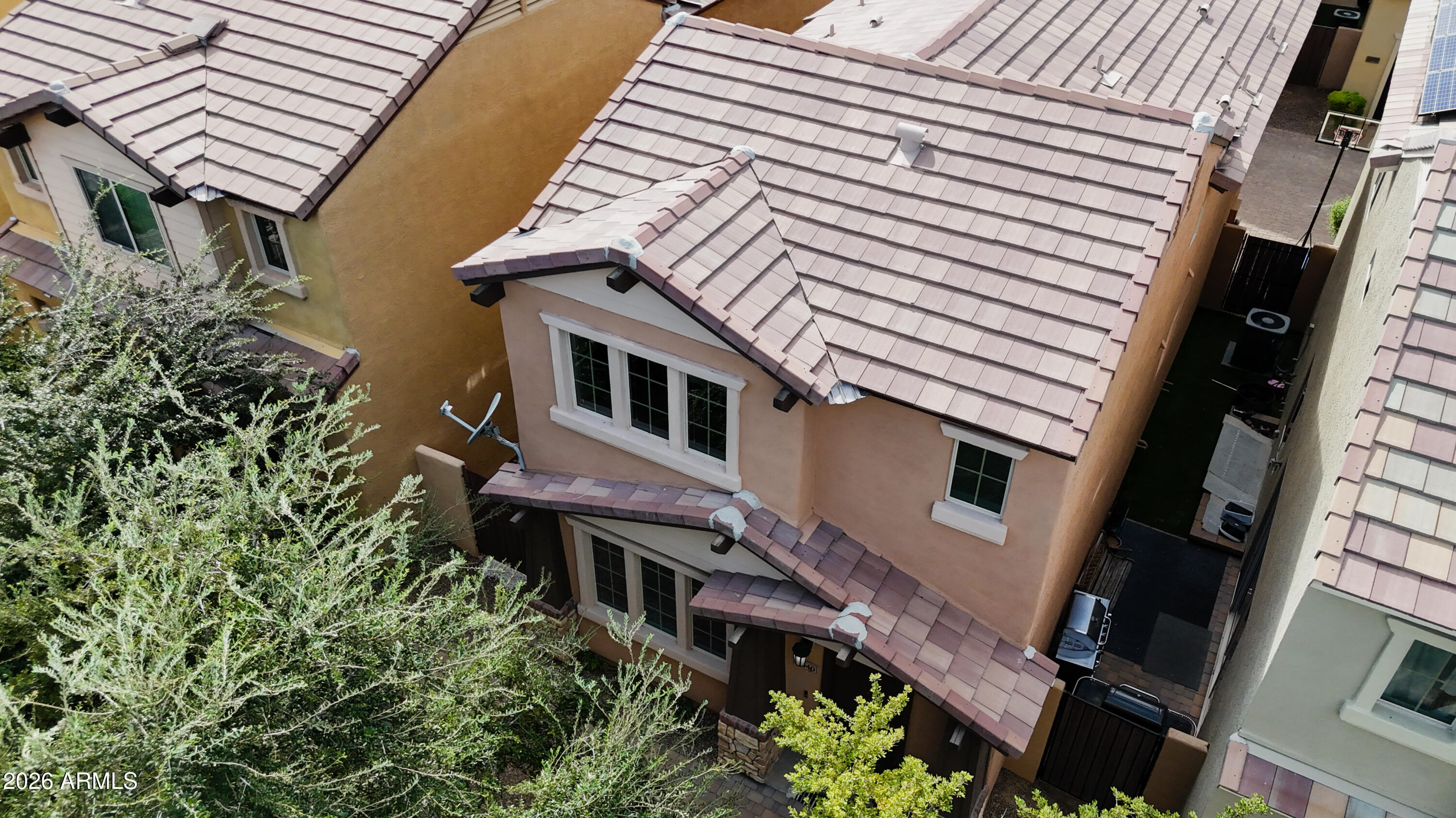 Aerial view of a two-story stucco home with a pale tiled roof and trees partly obscuring the front.