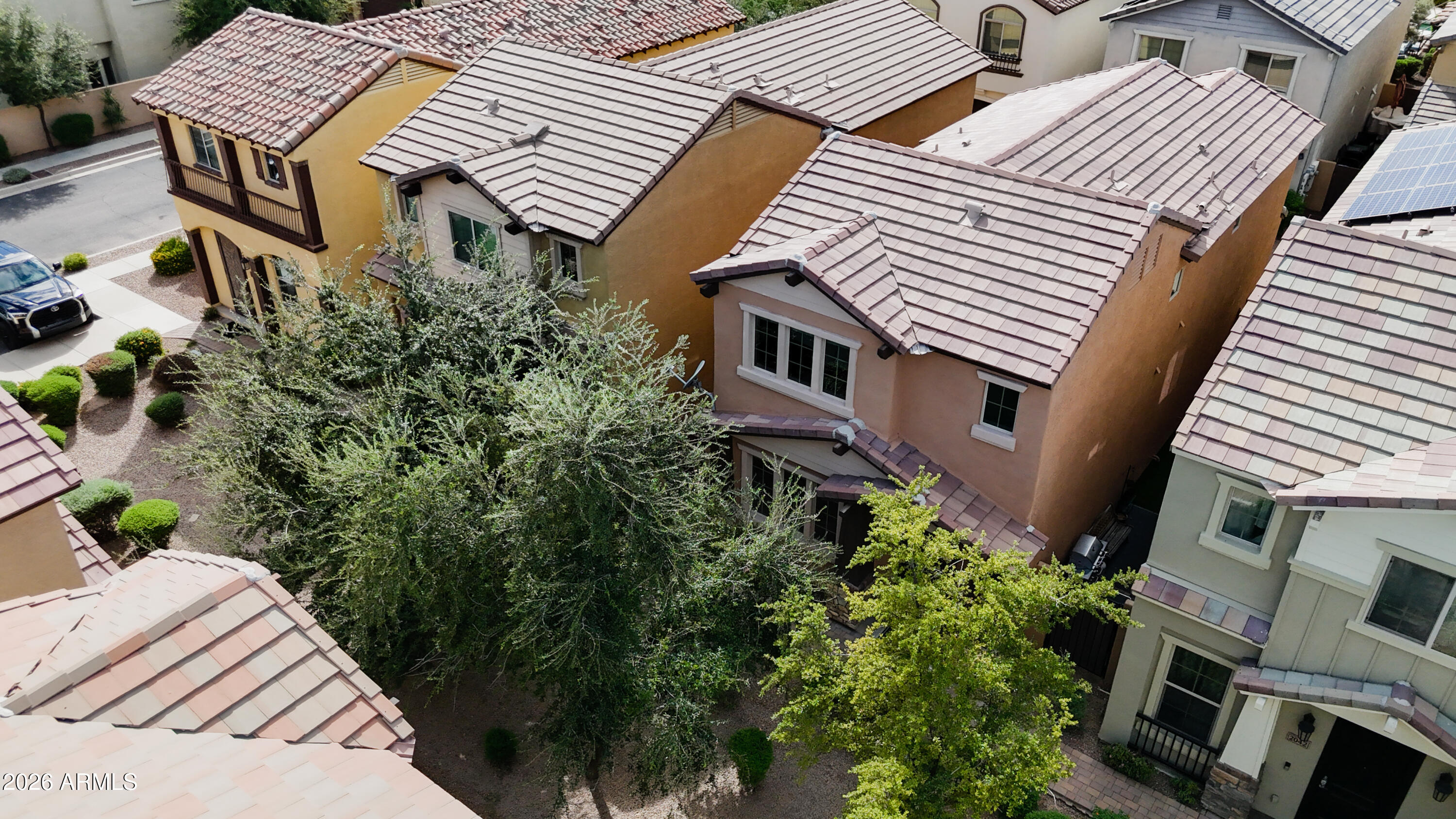 Aerial view of a tan two-story home with a tiled roof and mature trees among neighboring houses.