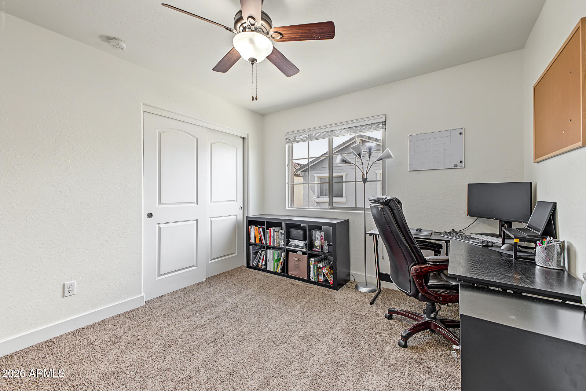 Home office with a black desk and chair, bookcase, carpet, and window.