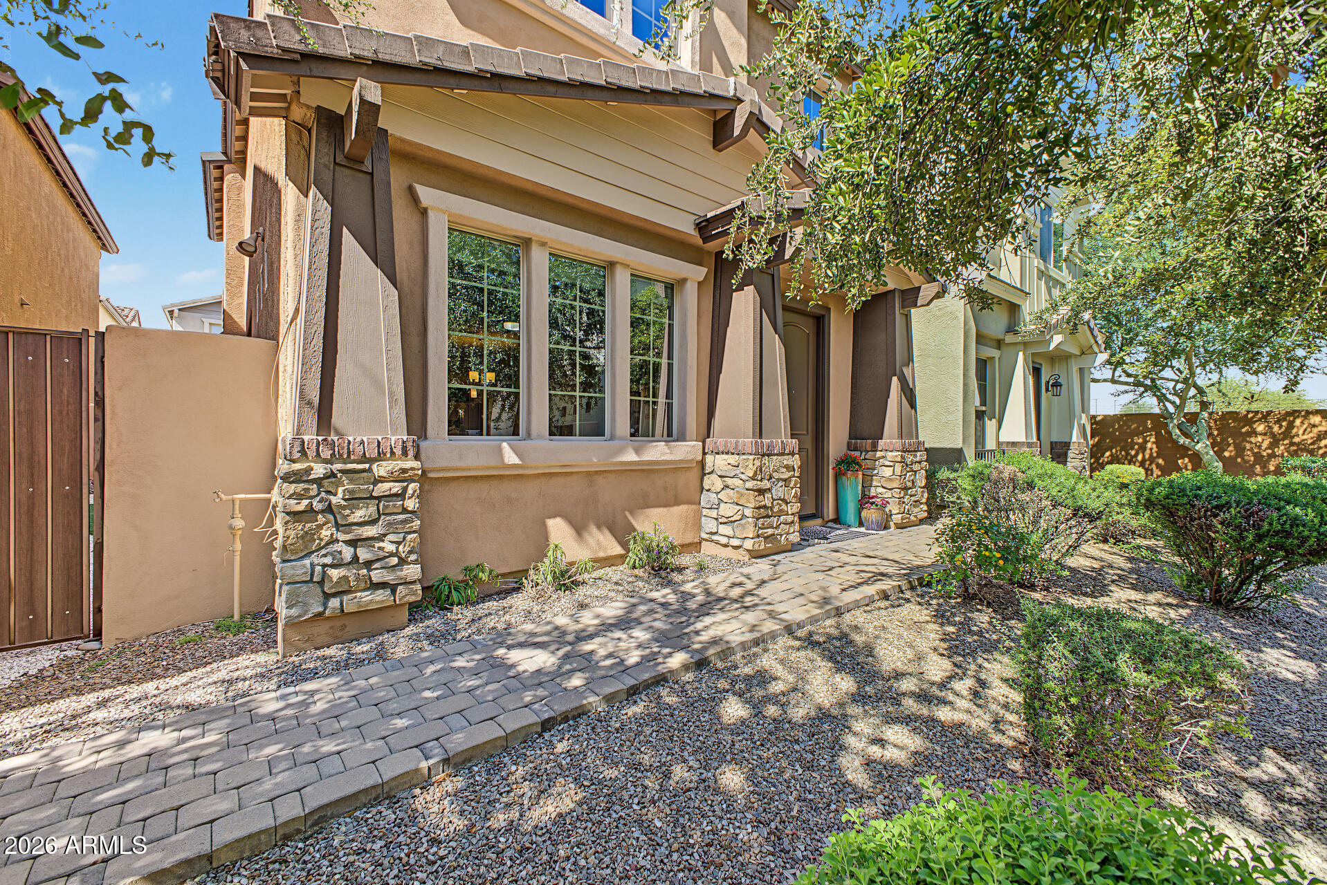 Tan stucco home with stone accents and a paved walkway through landscaped gravel.