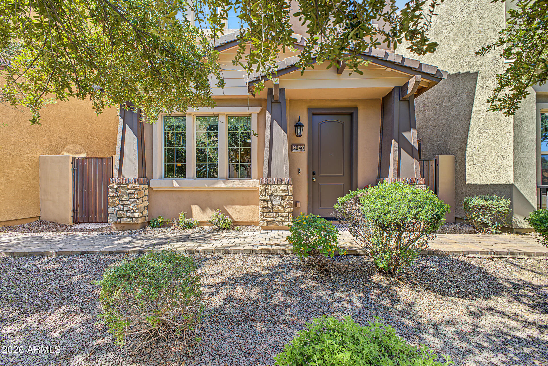 Home entrance with a covered porch, stone accents, and a gravel yard shaded by trees.