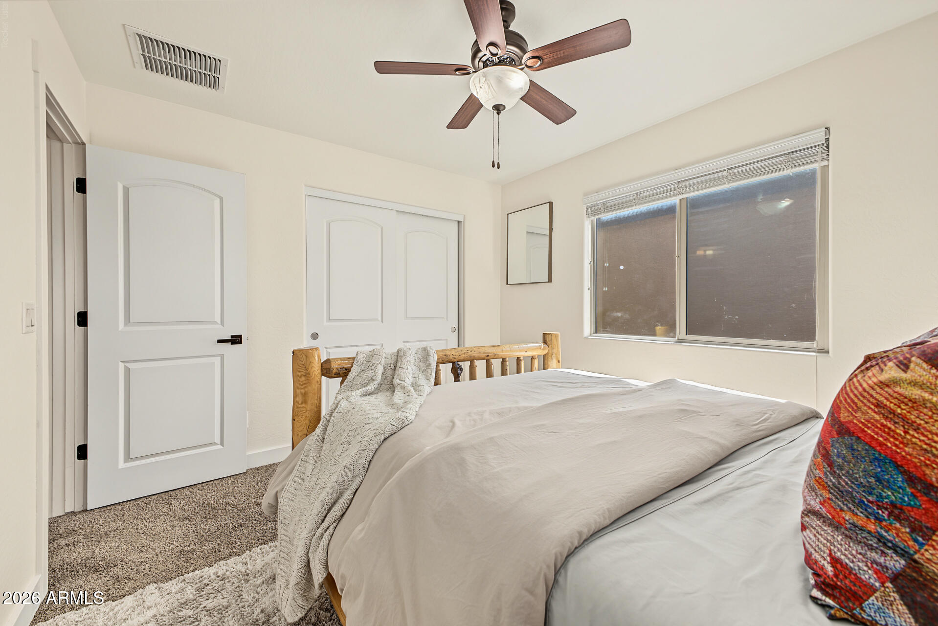 Bedroom with a wooden bed, white bedding, ceiling fan, and window with blinds.