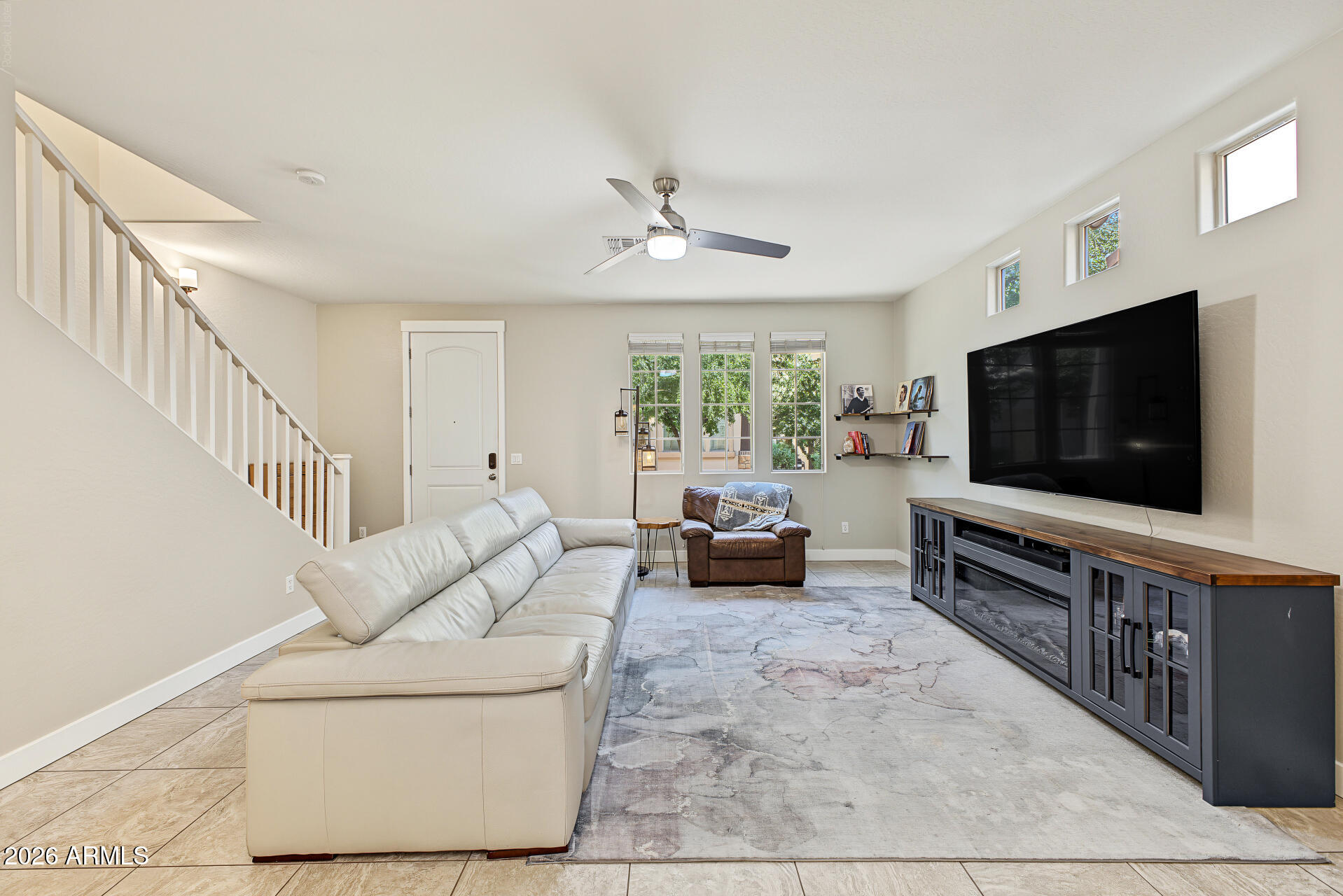 Living room with a cream sectional, large television, staircase, and tall windows.