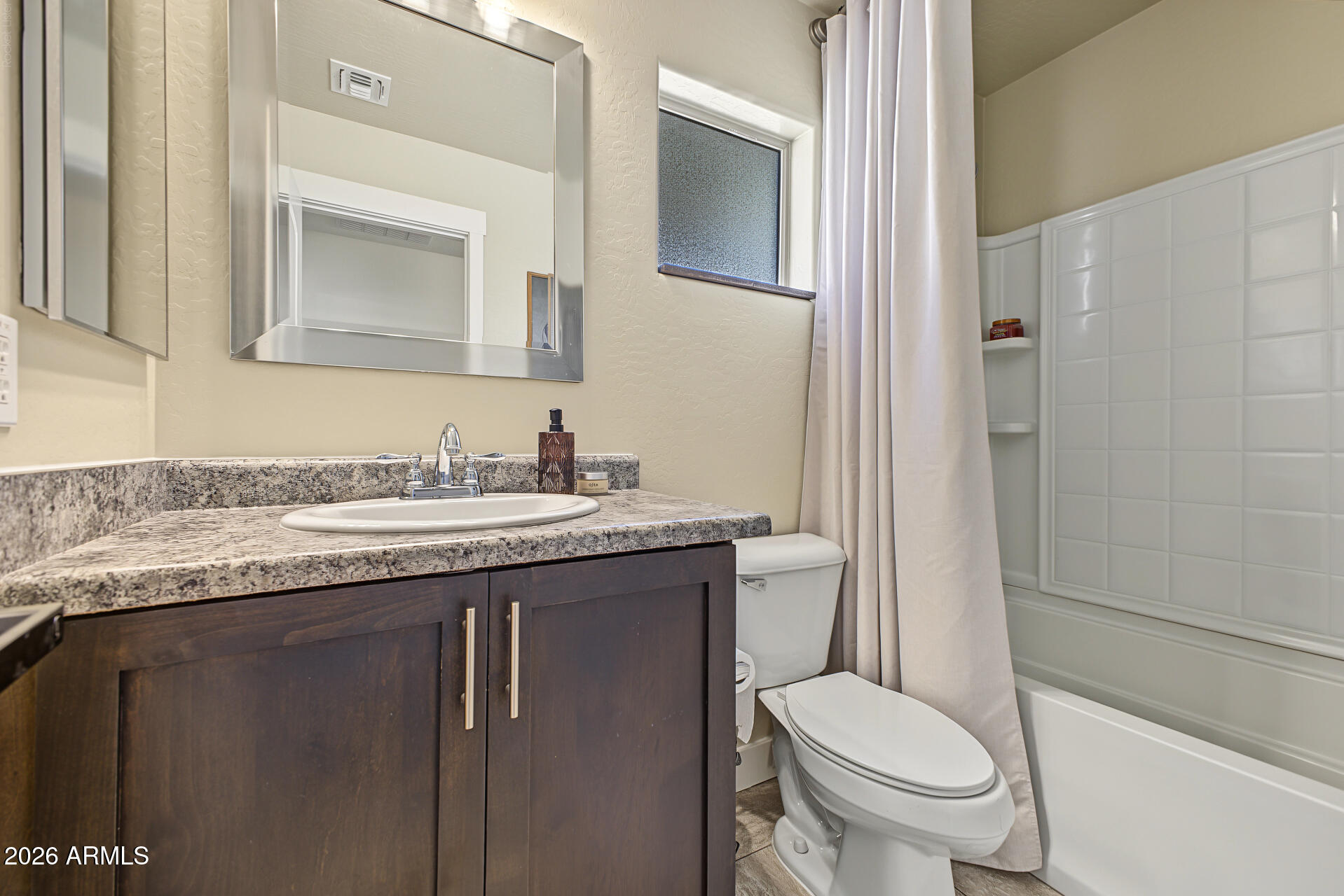 Bathroom with a dark wood vanity and speckled countertop beside a tiled tub-shower.