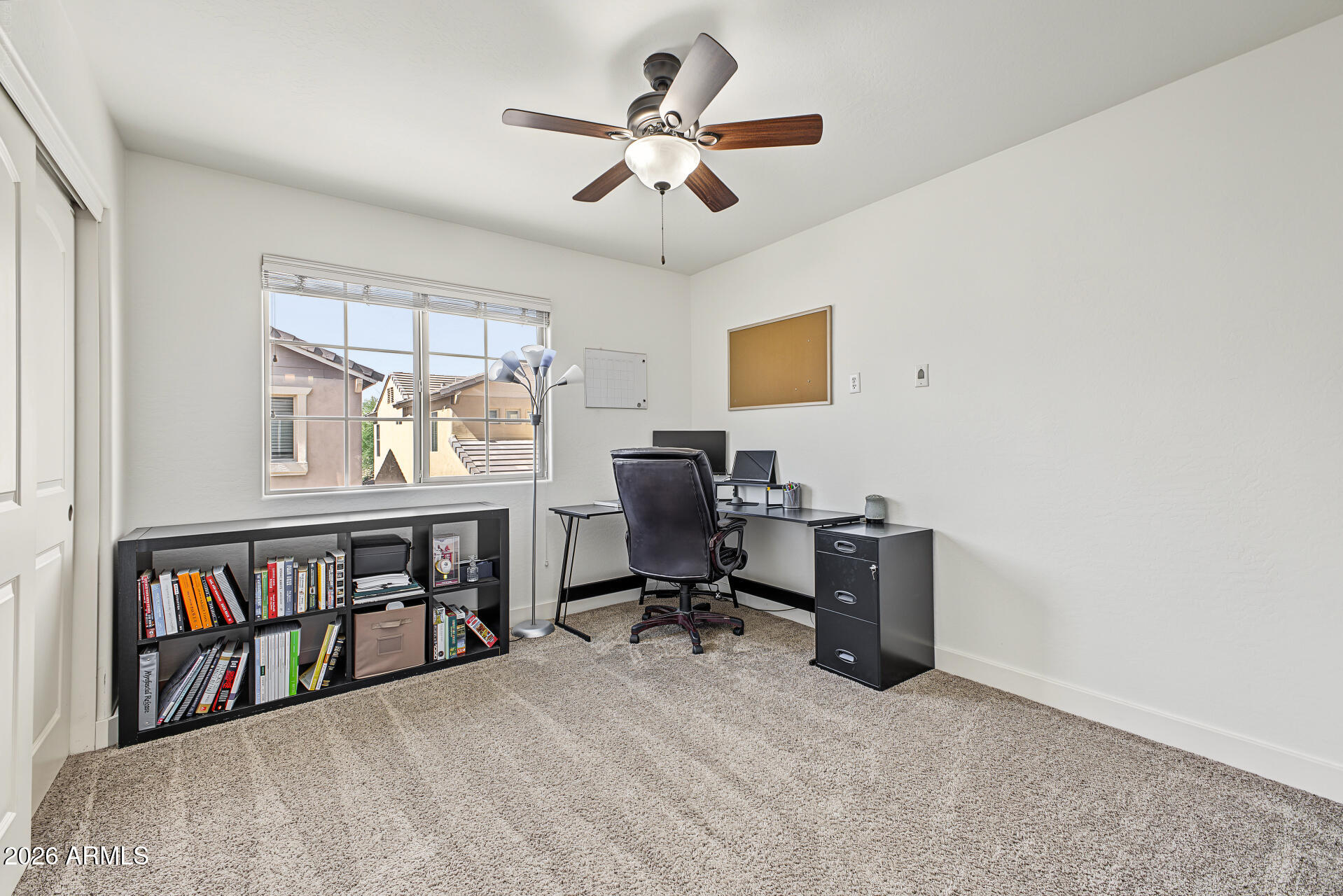 Furnished home office with a black desk and bookcase beside a large window.