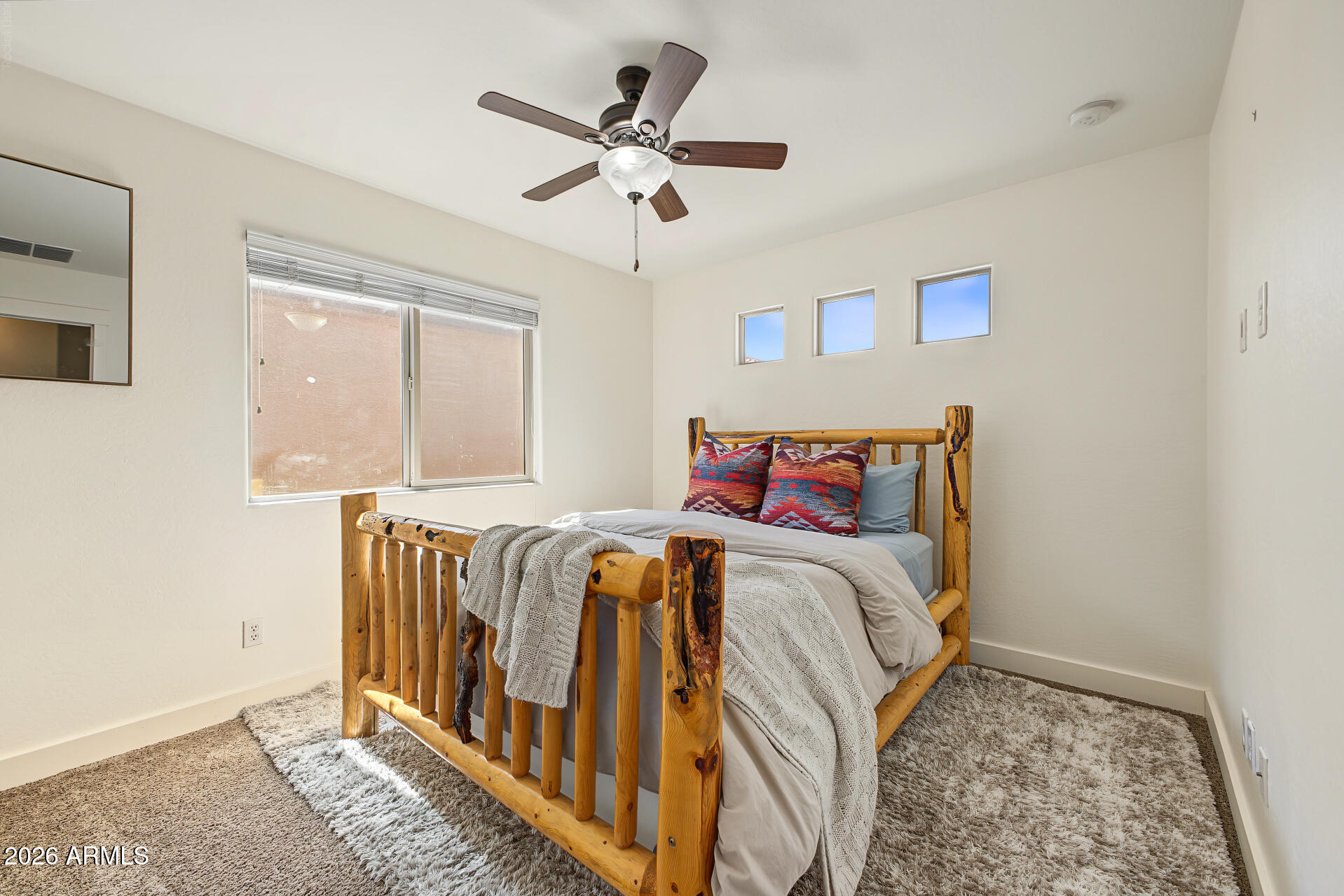 Furnished bedroom with a rustic log bed, patterned pillows, and three high windows.
